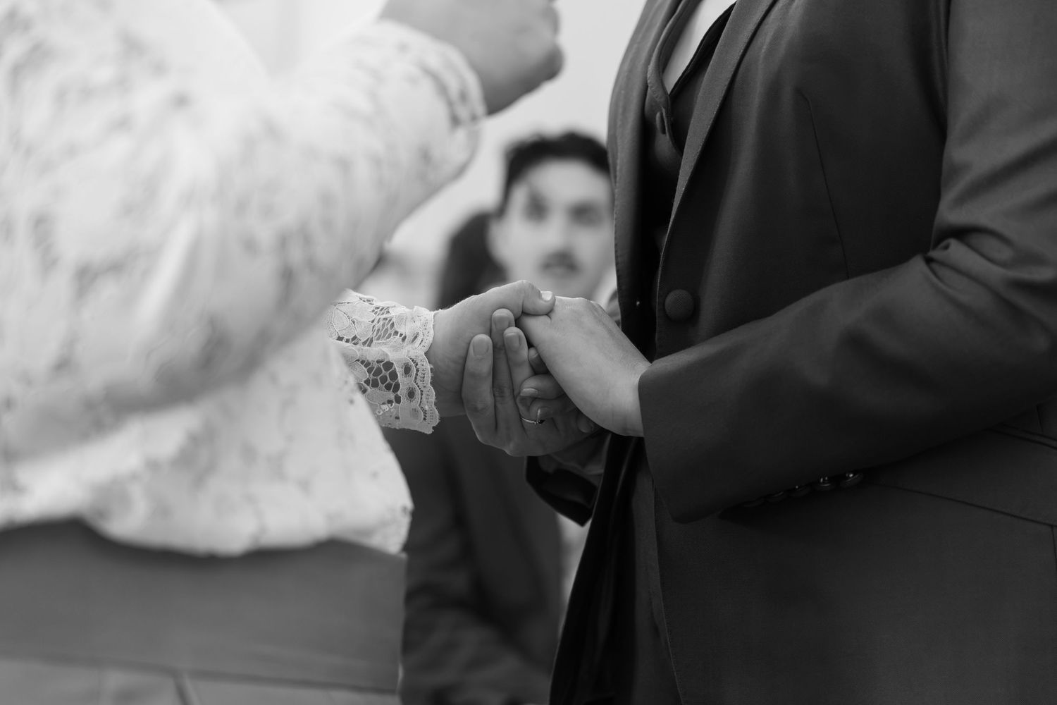 Black and white wedding ceremony photo of groom holding bride's hands at the altar.