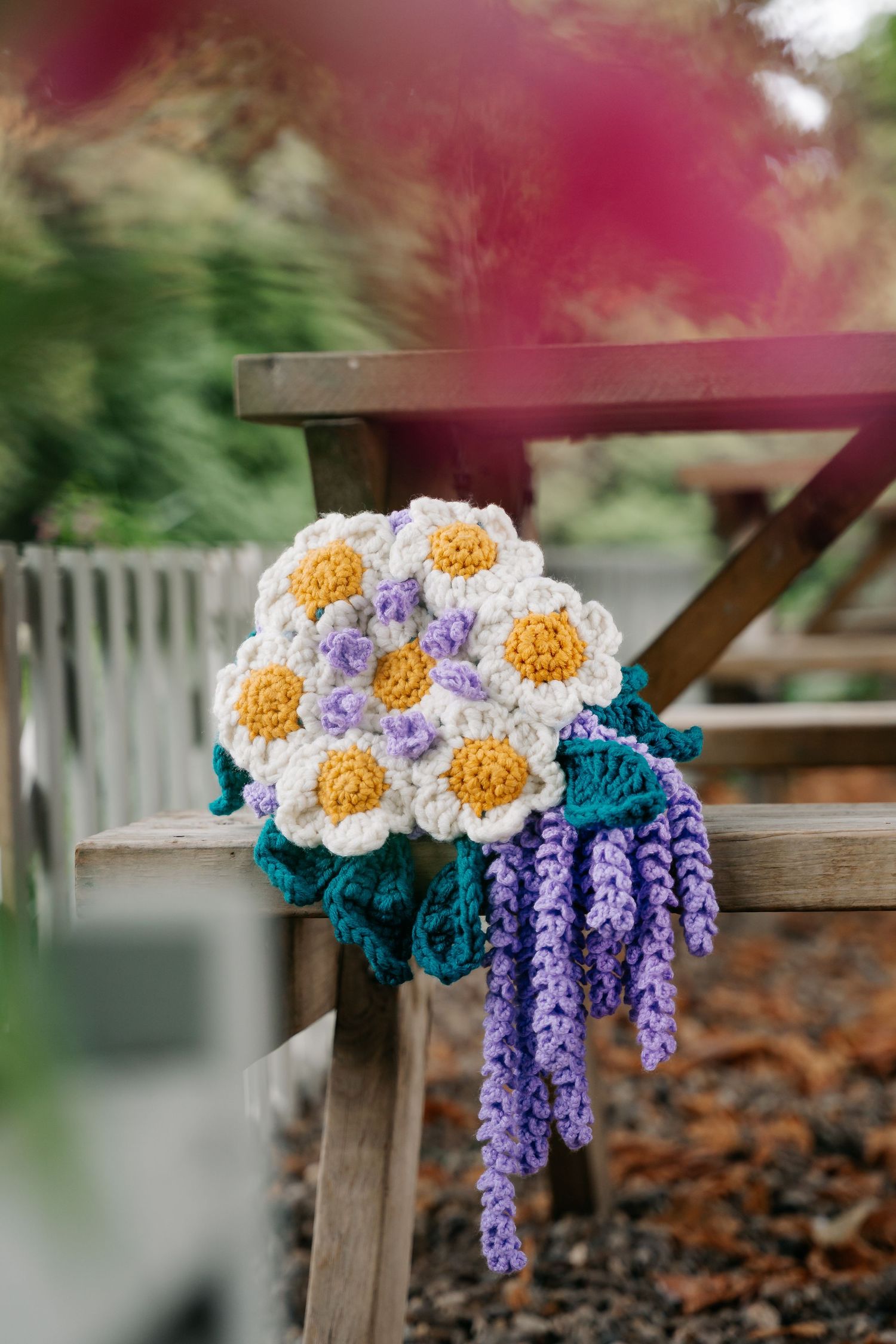 Handmade crochet flower bouquet with white daisy and purple lavender flowers displayed on a wooden chair outdoors.