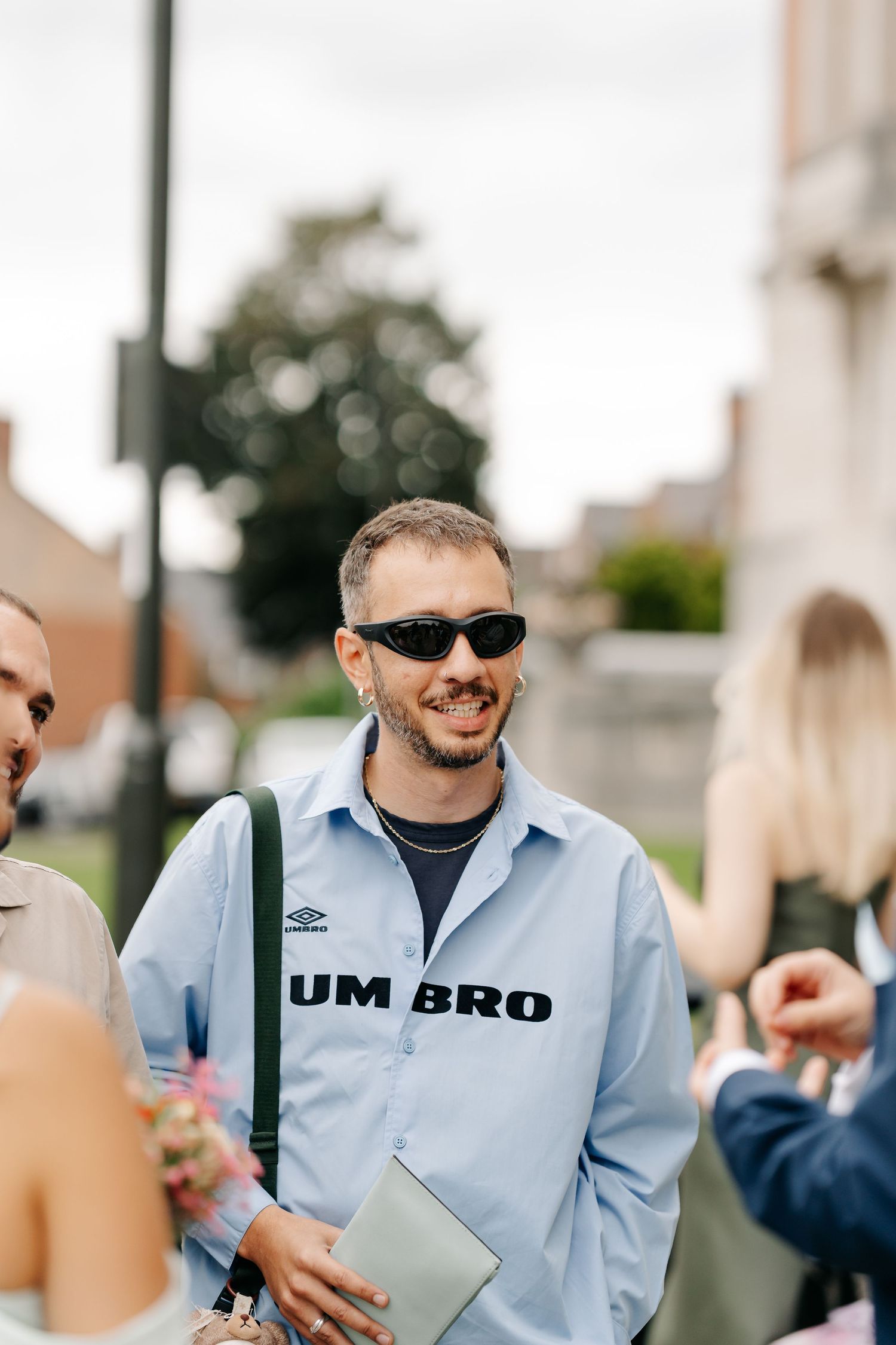 Man wearing Umbro shirt and black sunglasses smiling outdoors at a casual gathering.