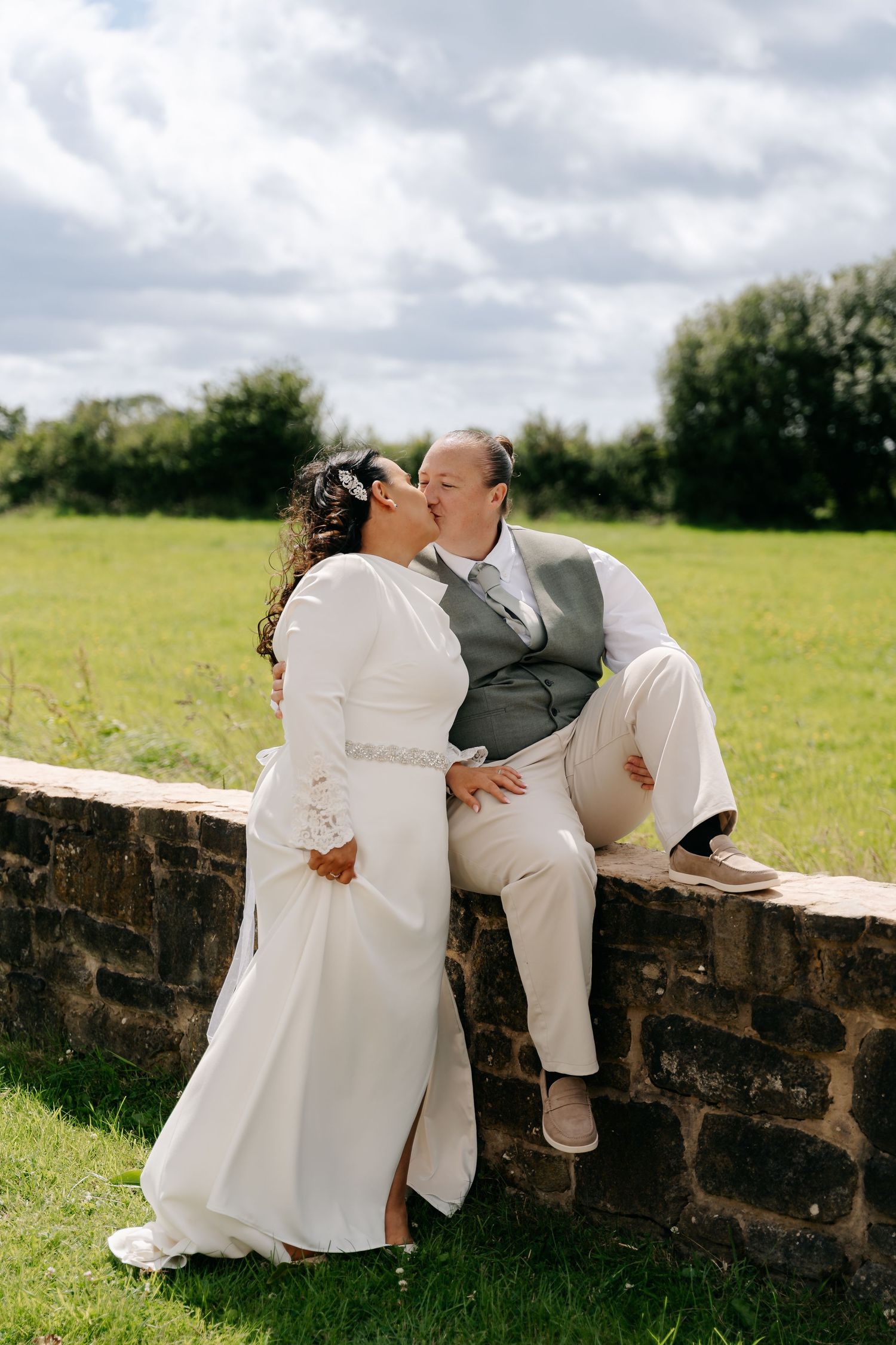 Bride and groom share a romantic kiss on a stone wall outdoors on their wedding day.
