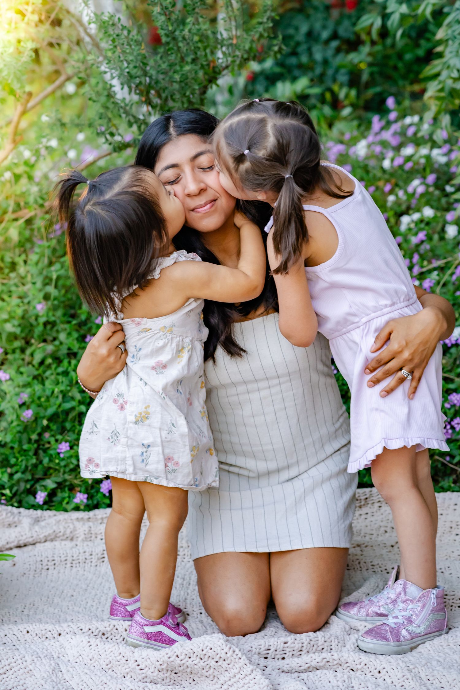 girls kissing their mom on each cheek while sunshine streams in from behind