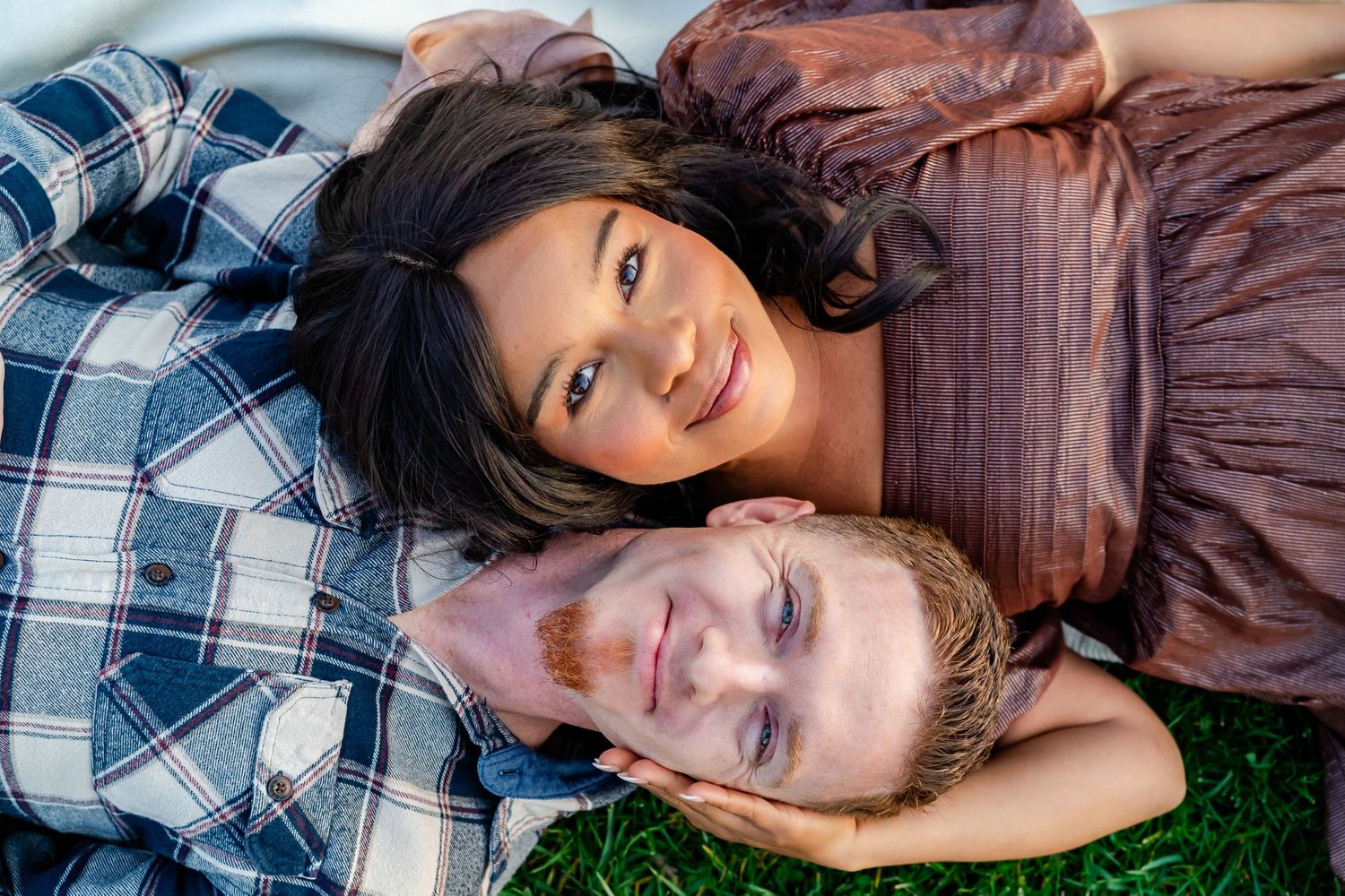 husband and wife lay on blanket and look up at the camera
