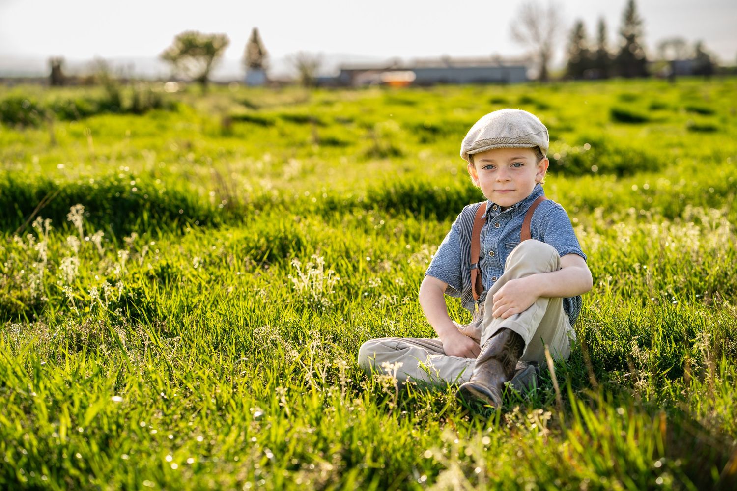 portrait of young boy sitting in a green field with suspenders