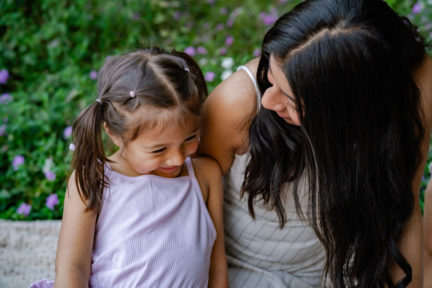 mom and daughter laugh together with flowers in the background