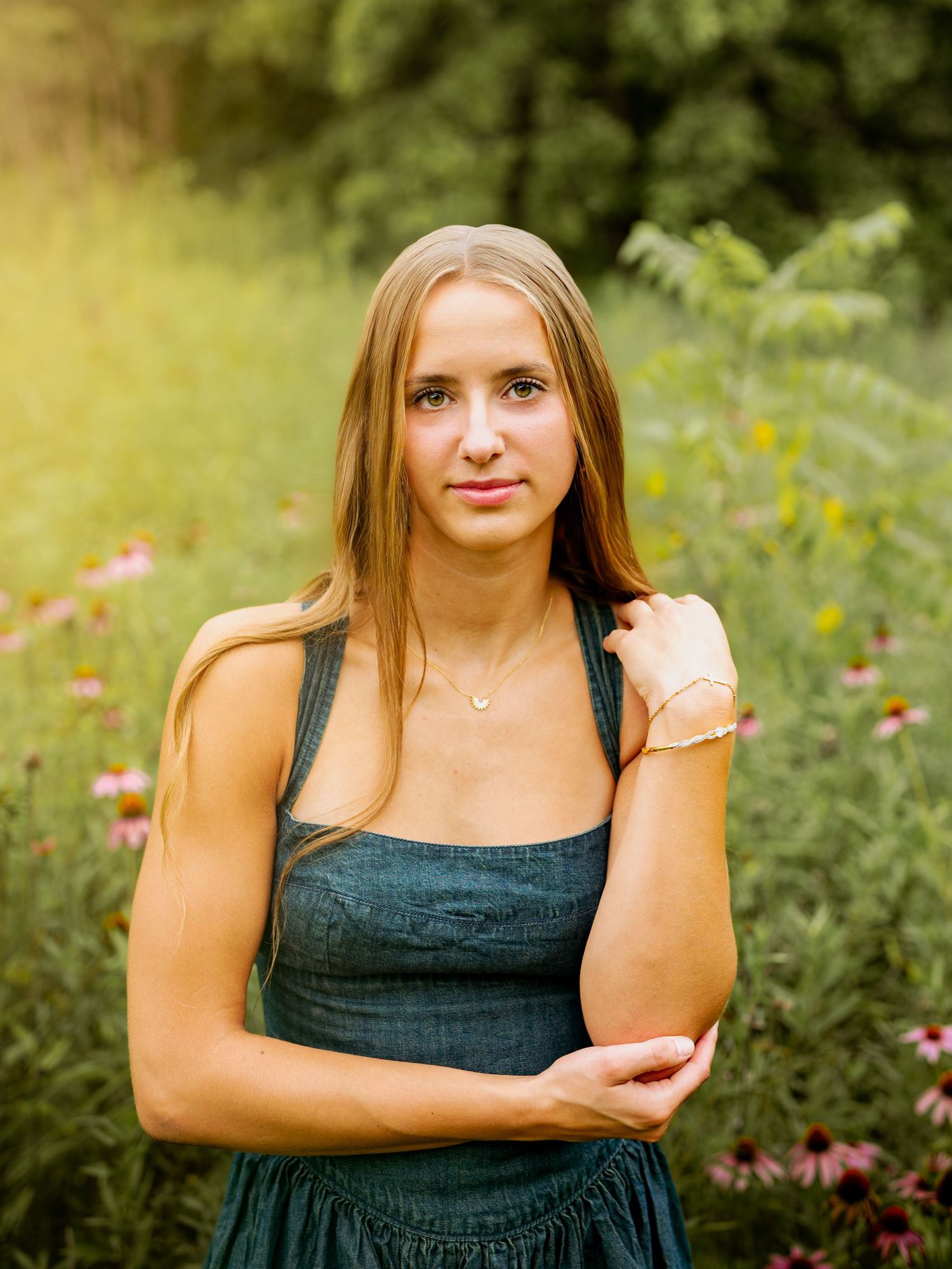 A person in a black sleeveless dress poses outdoors in a garden with pink flowers in the background.