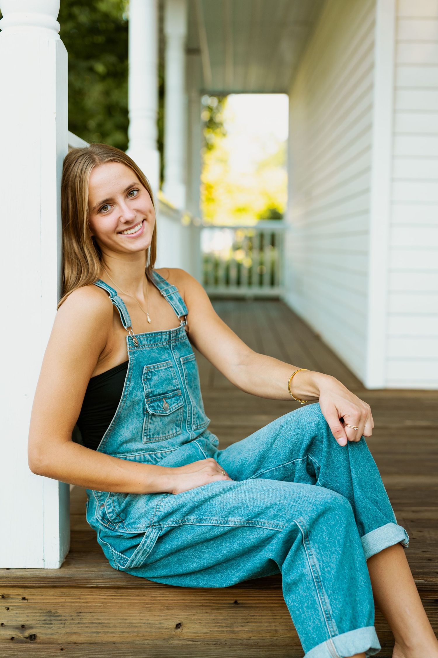 A casual portrait series showing someone in denim overalls sitting on a wooden porch in natural lighting.