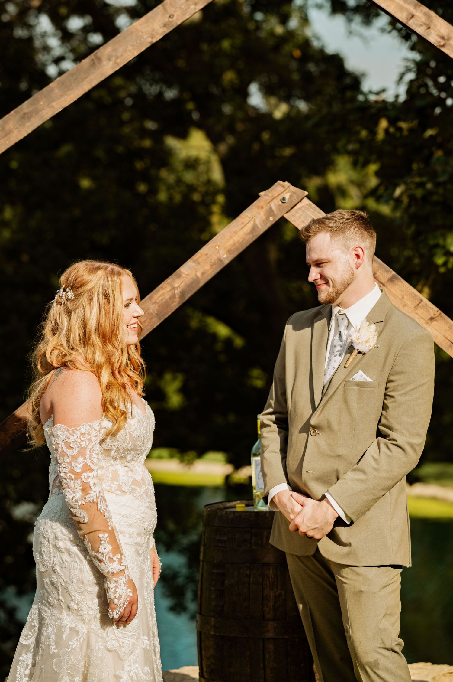 Wedding couple poses together against rustic wooden beams in warm golden sunlight.