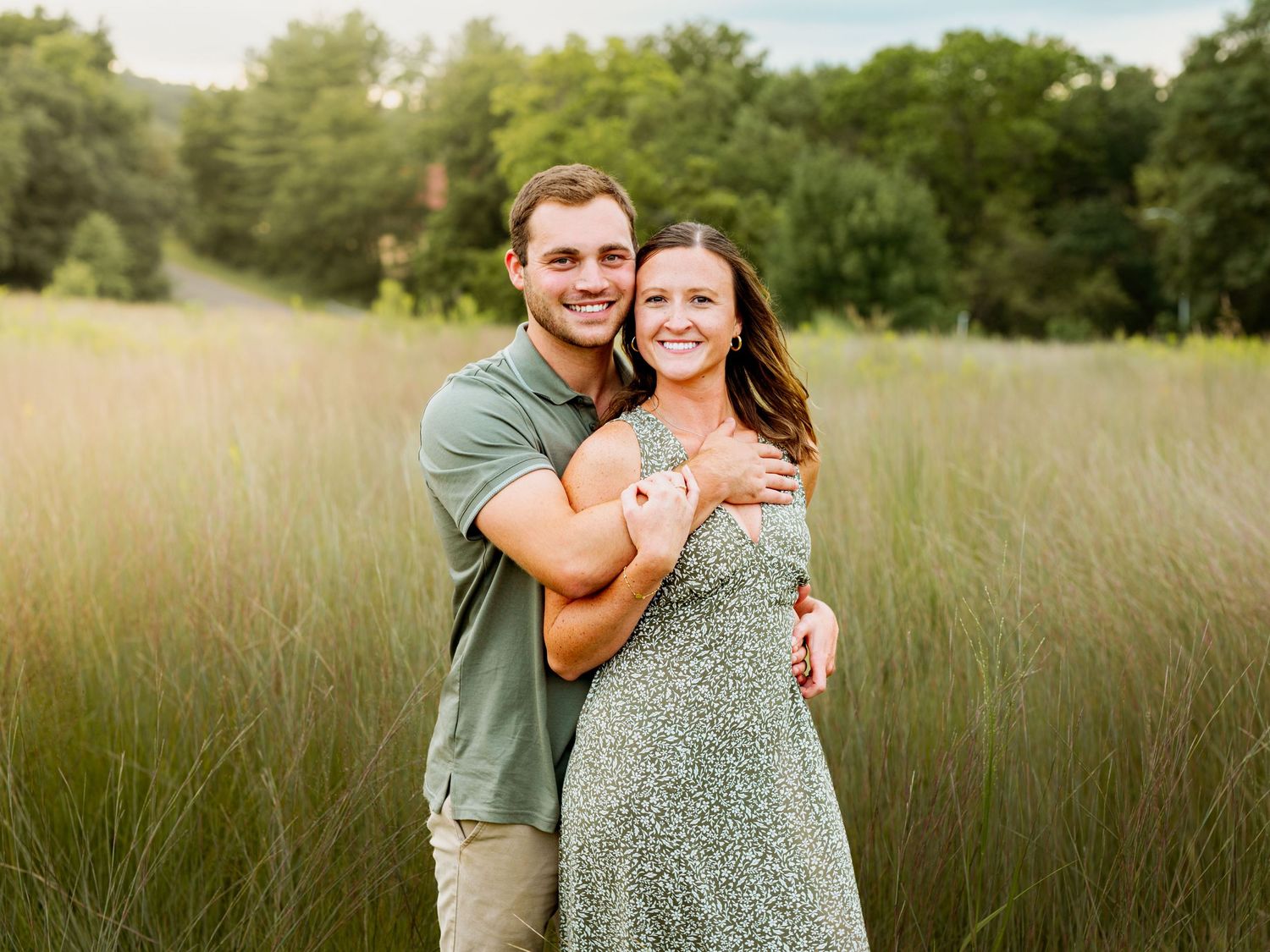 A couple embraces while standing in a sunlit field of tall grass during golden hour.