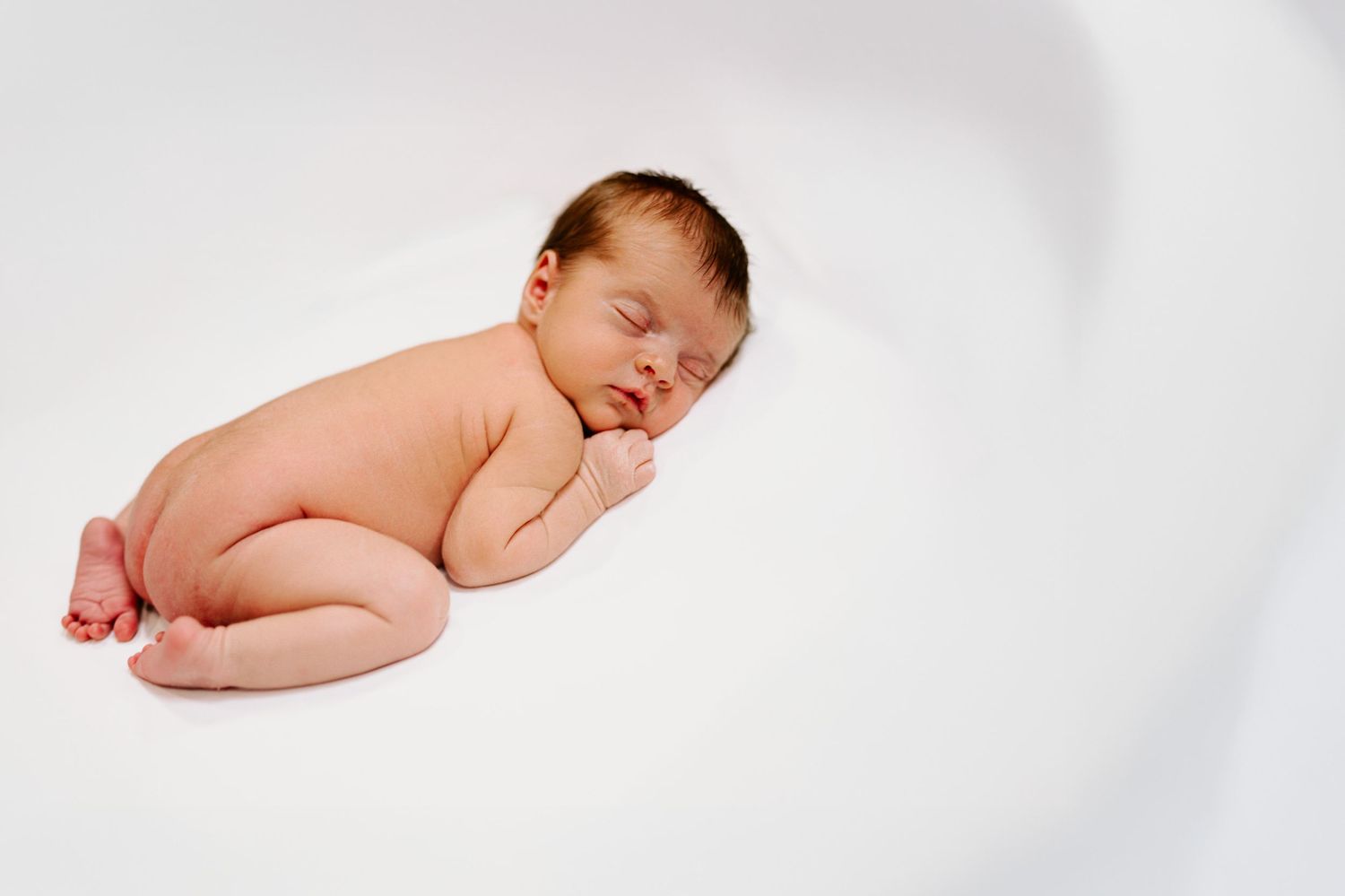 Sleeping newborn baby in fetal position on white background.