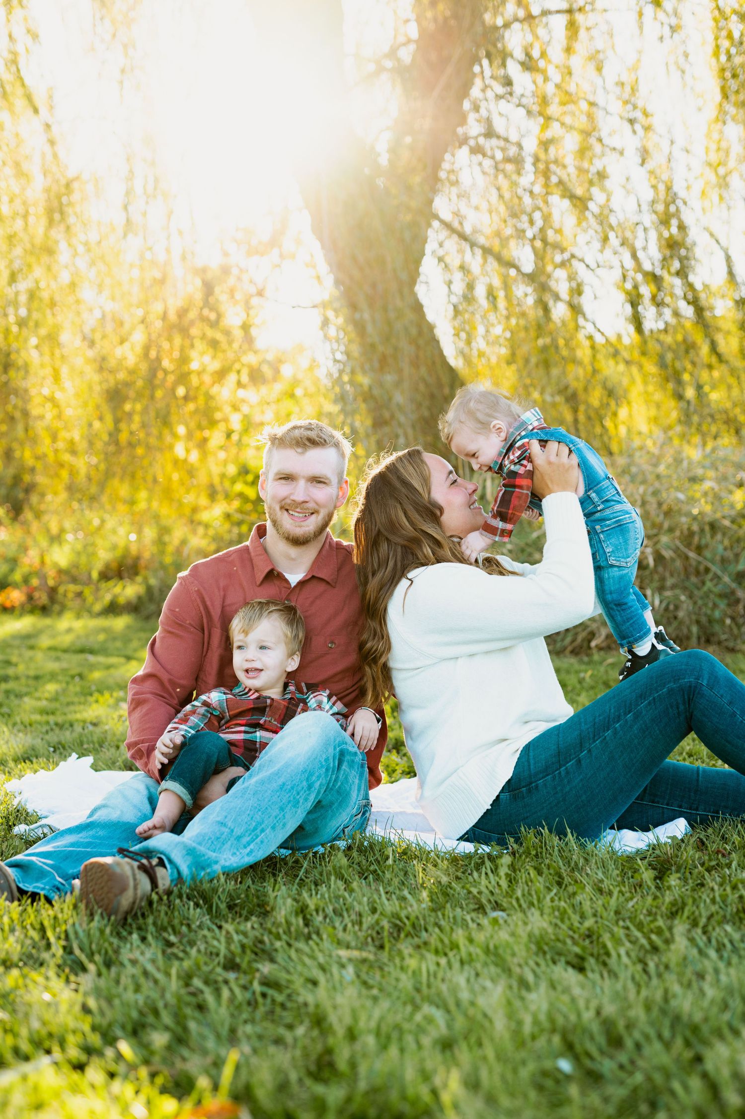 Family enjoying playful moments together while laying on grass during golden hour sunset.