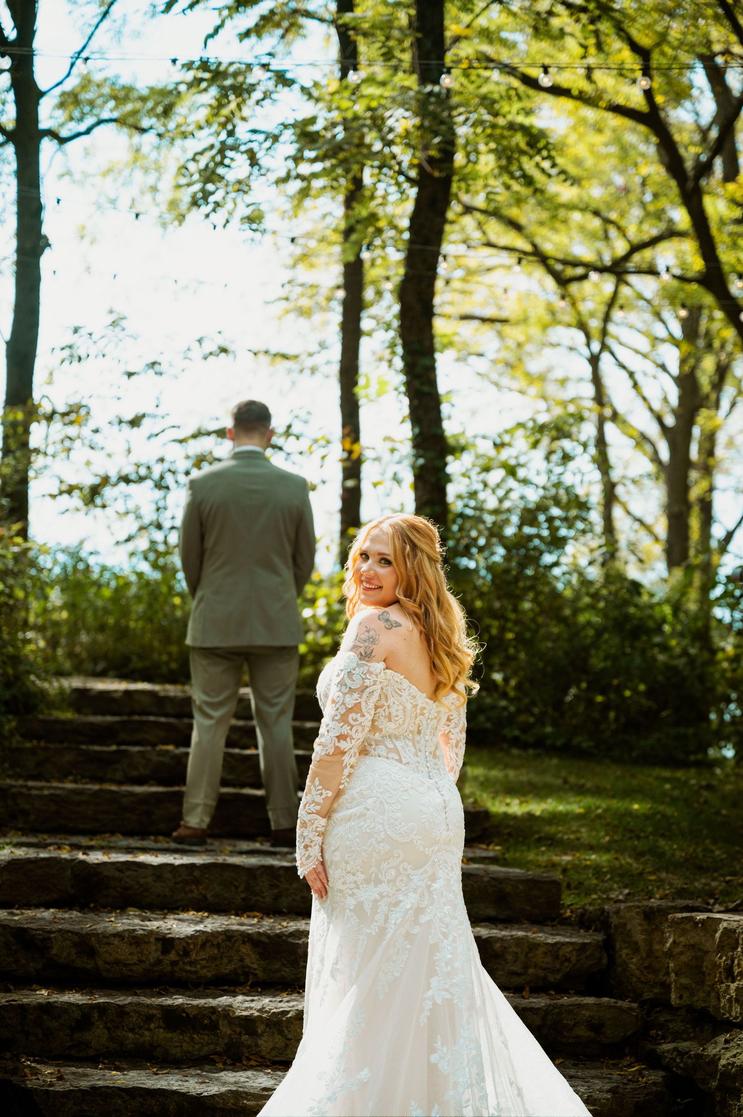 A romantic wedding photo on stone steps surrounded by lush trees and natural sunlight.