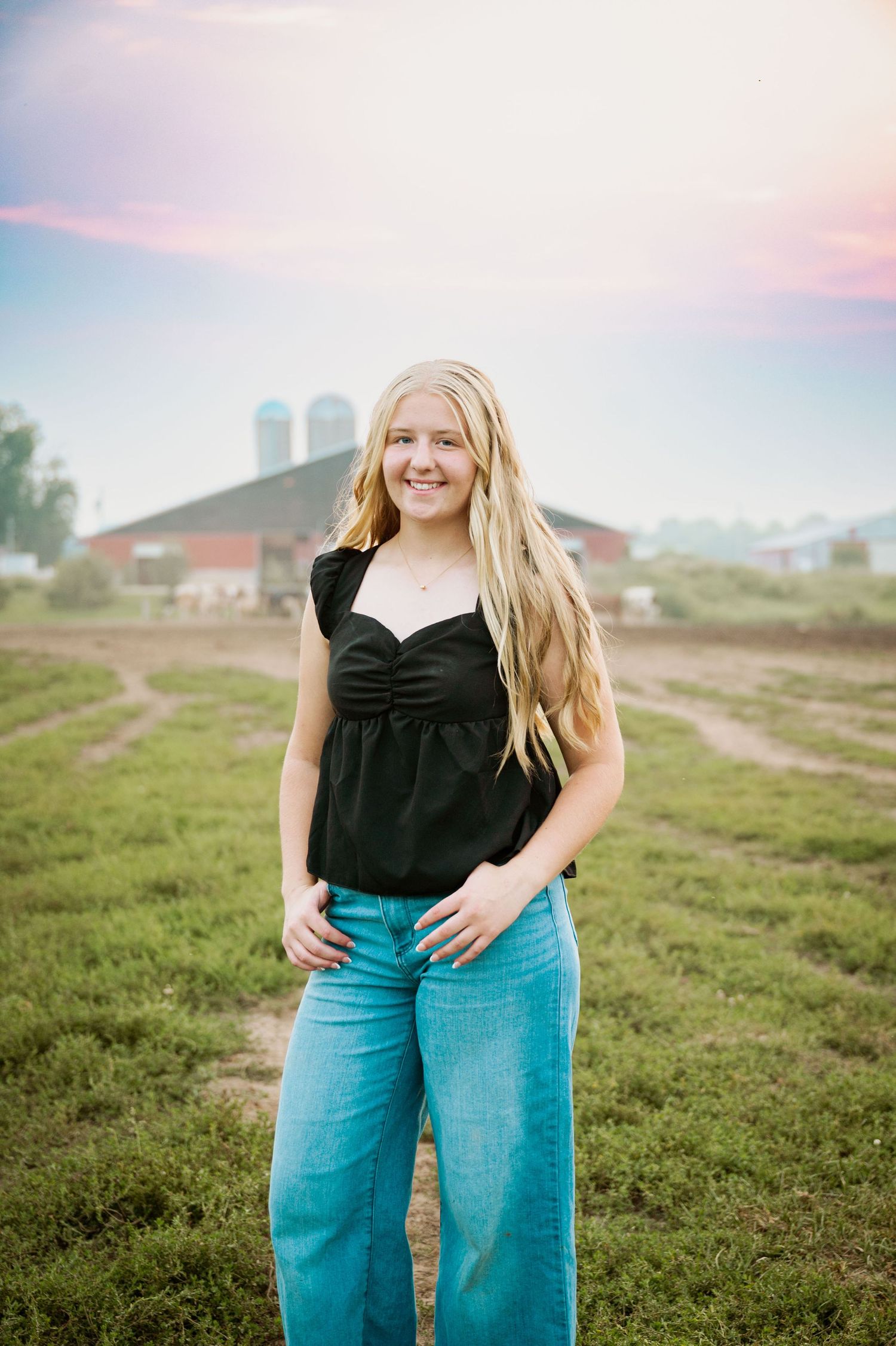 Outdoor portrait session on a farm with buildings and silos visible in the distance.