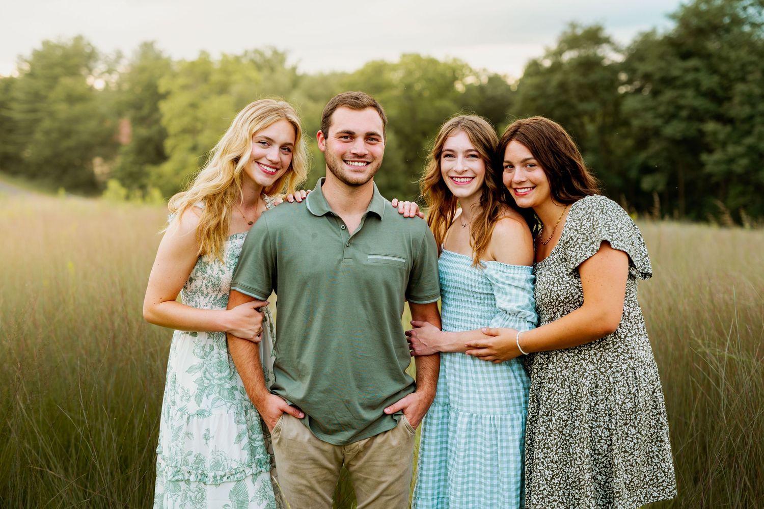A group poses together outdoors in coordinating casual outfits against a natural grassy field backdrop.