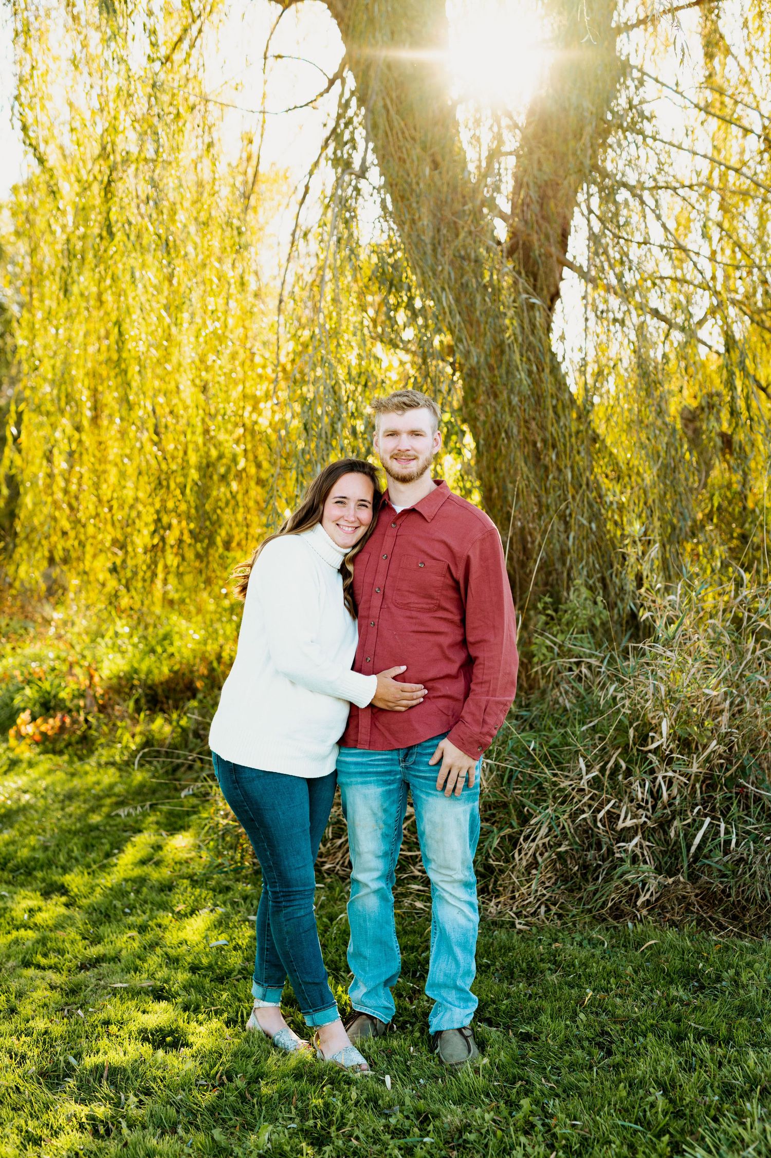 A couple embraces under a willow tree with golden leaves on a sunny autumn day.