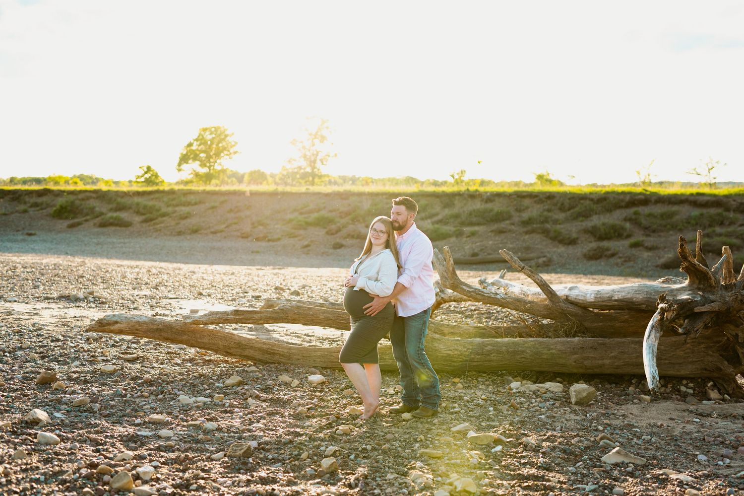 Two people walk along a rocky beach shoreline at sunset with golden sunlight streaming through the scene.
