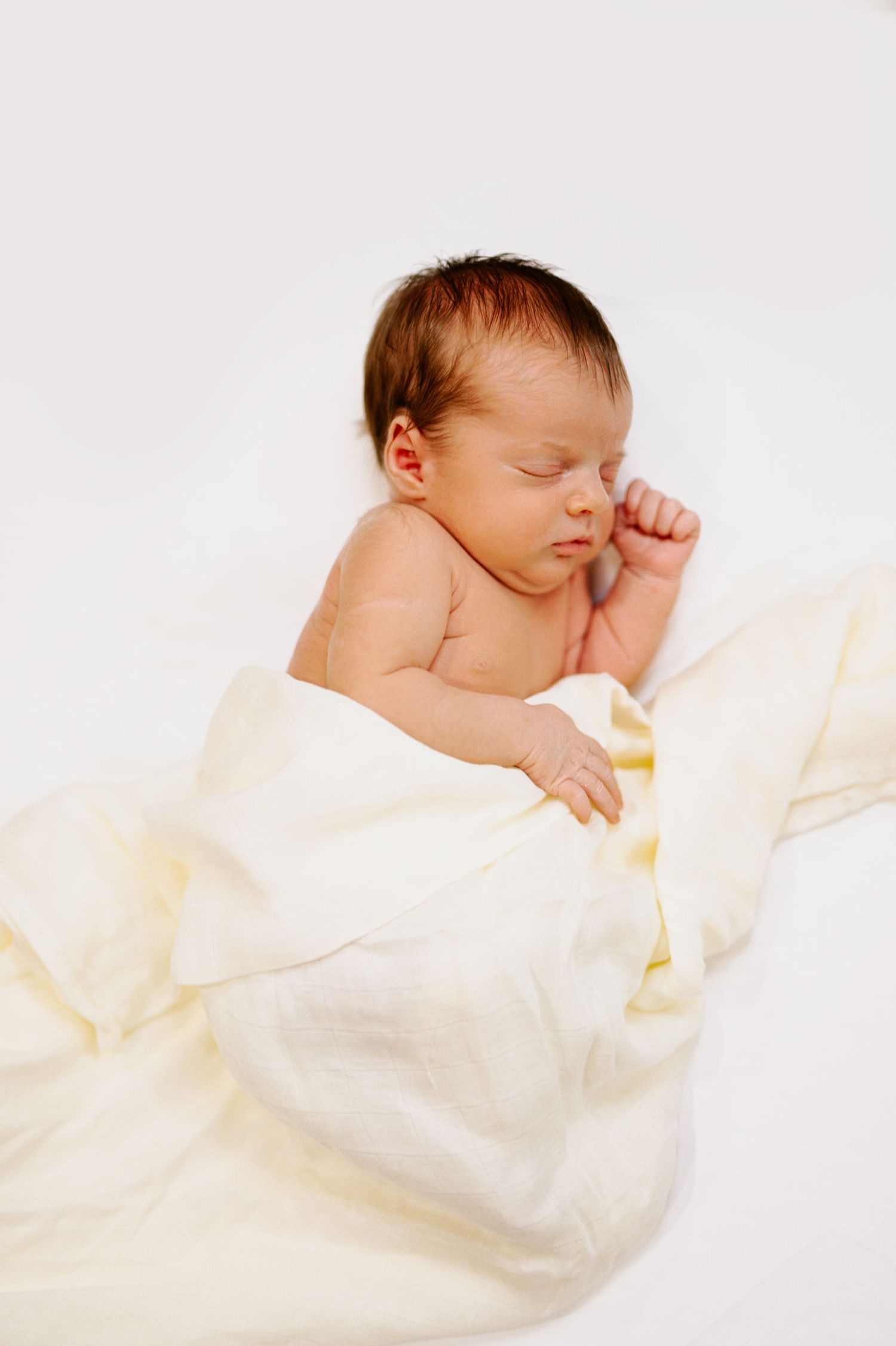 Peaceful newborn sleeping with cream blanket on white background.