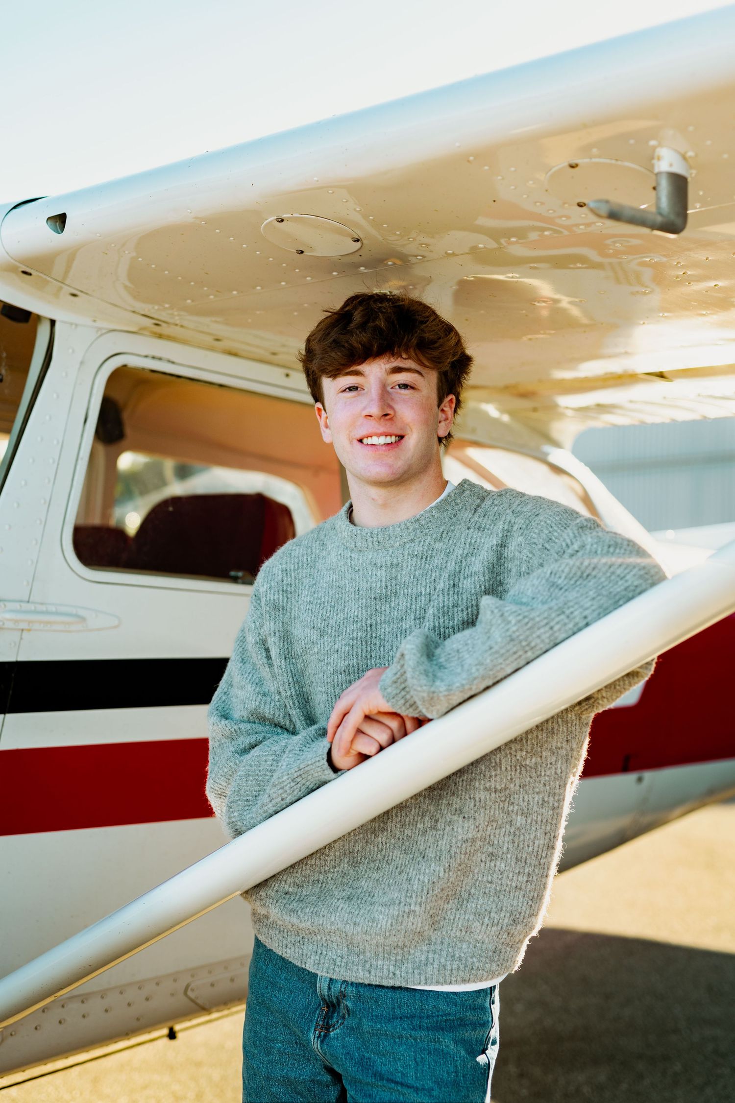 A series of photos showing someone in a gray sweater posing next to a small private aircraft on a sunny day.