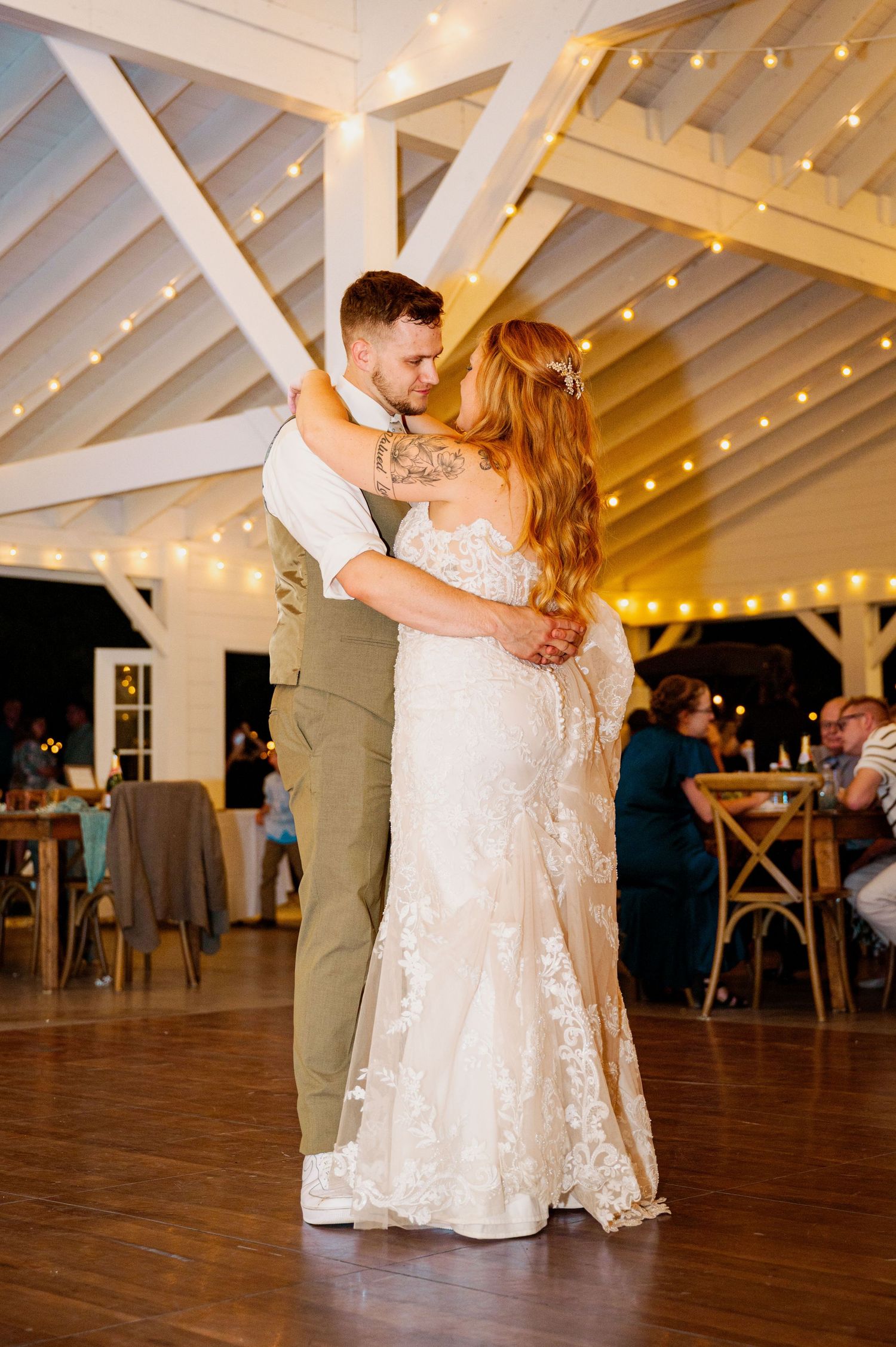 Couple sharing their first dance in an elegant white barn venue with string lights.