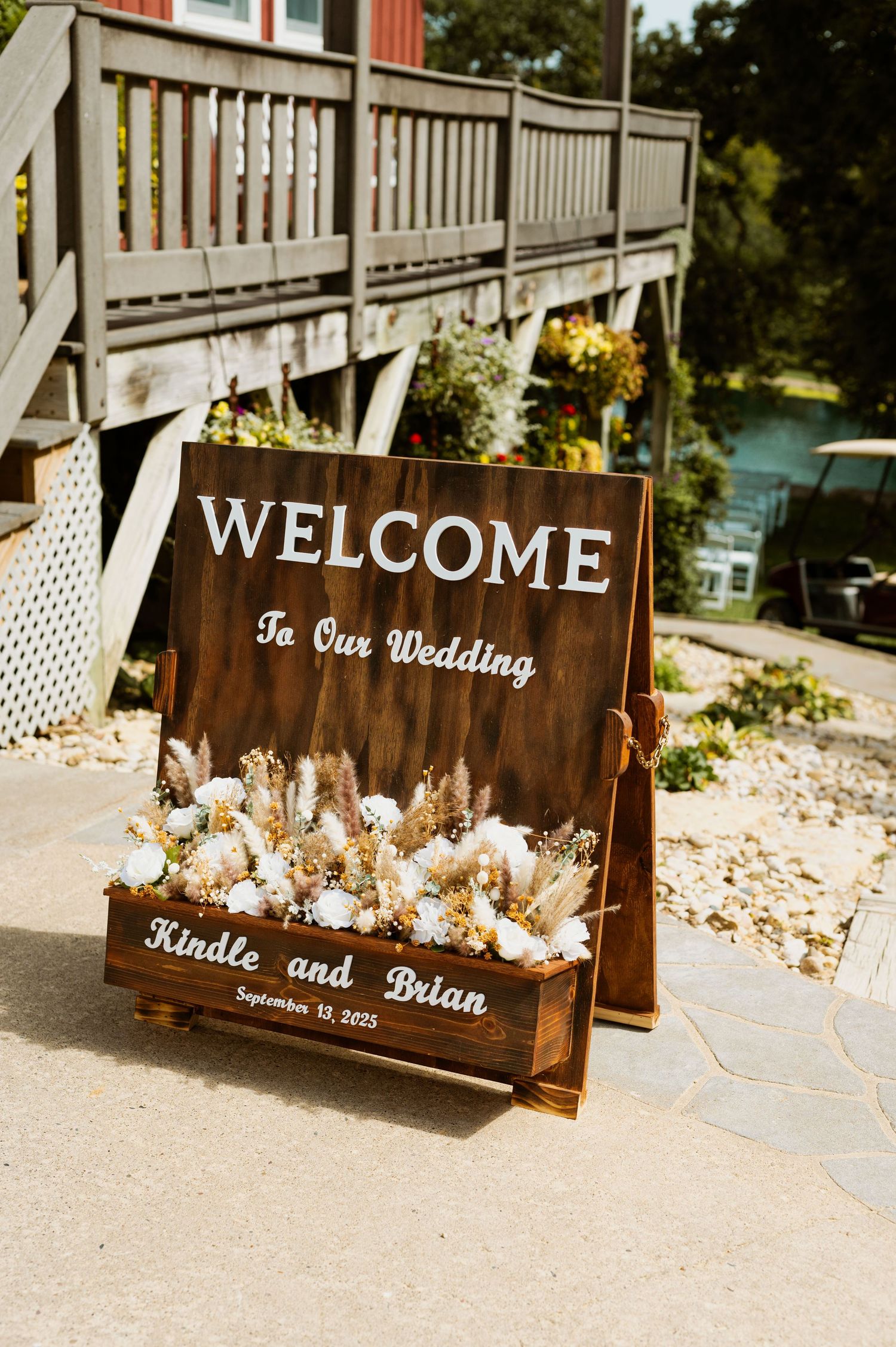 Wooden welcome signs decorated with floral arrangements displayed on a stone pathway for a wedding celebration.