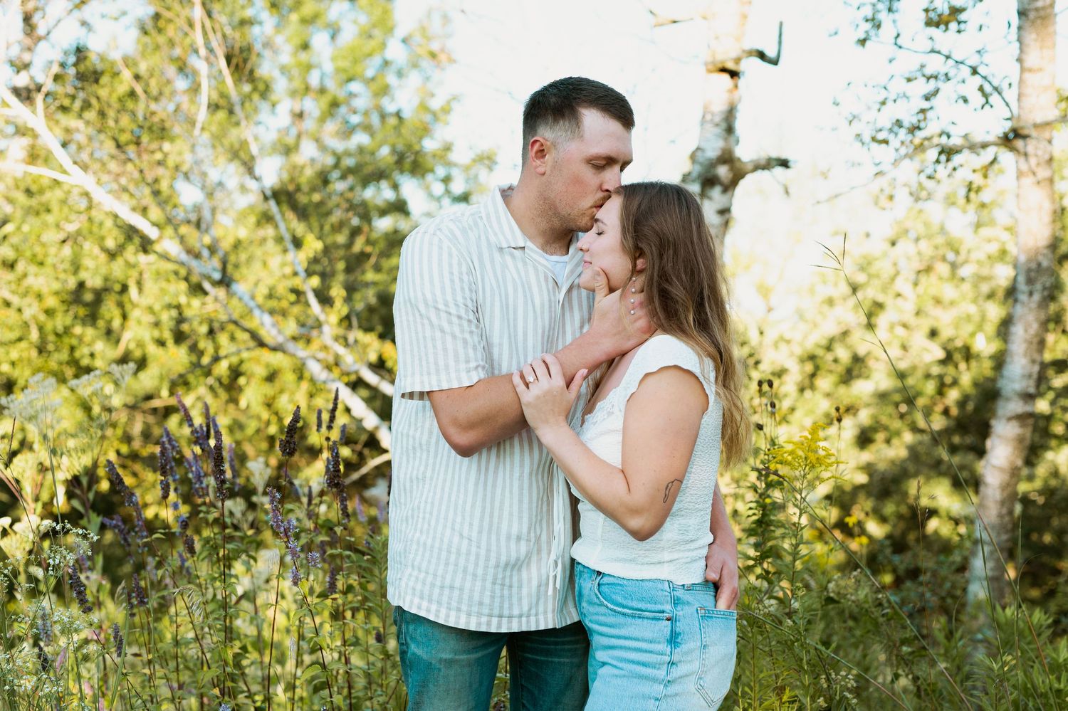 Couple sharing intimate moment among birch trees in sunlit forest setting.