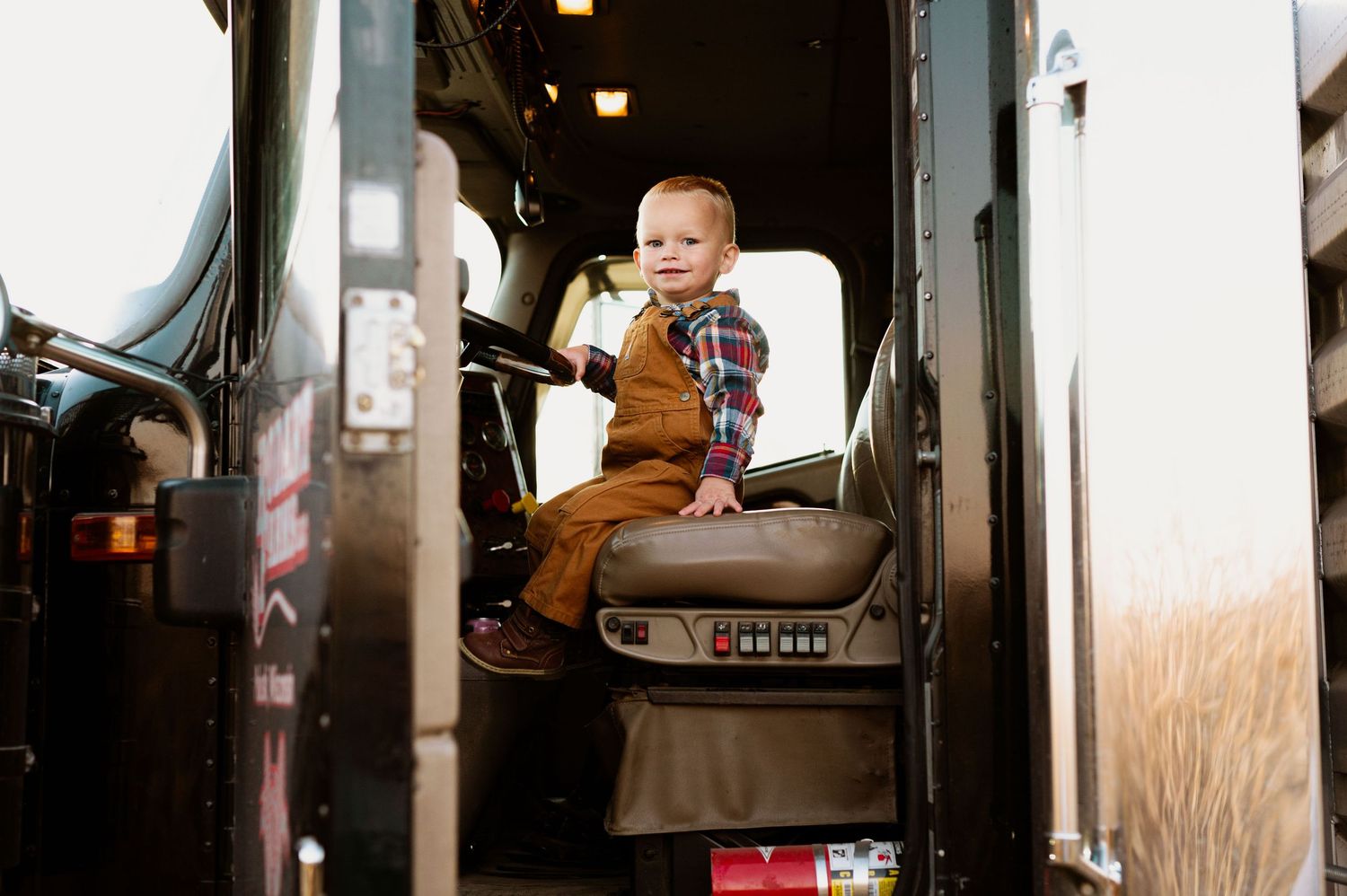 Inside view of a farm equipment cabin with controls and steering wheel against a dark background.