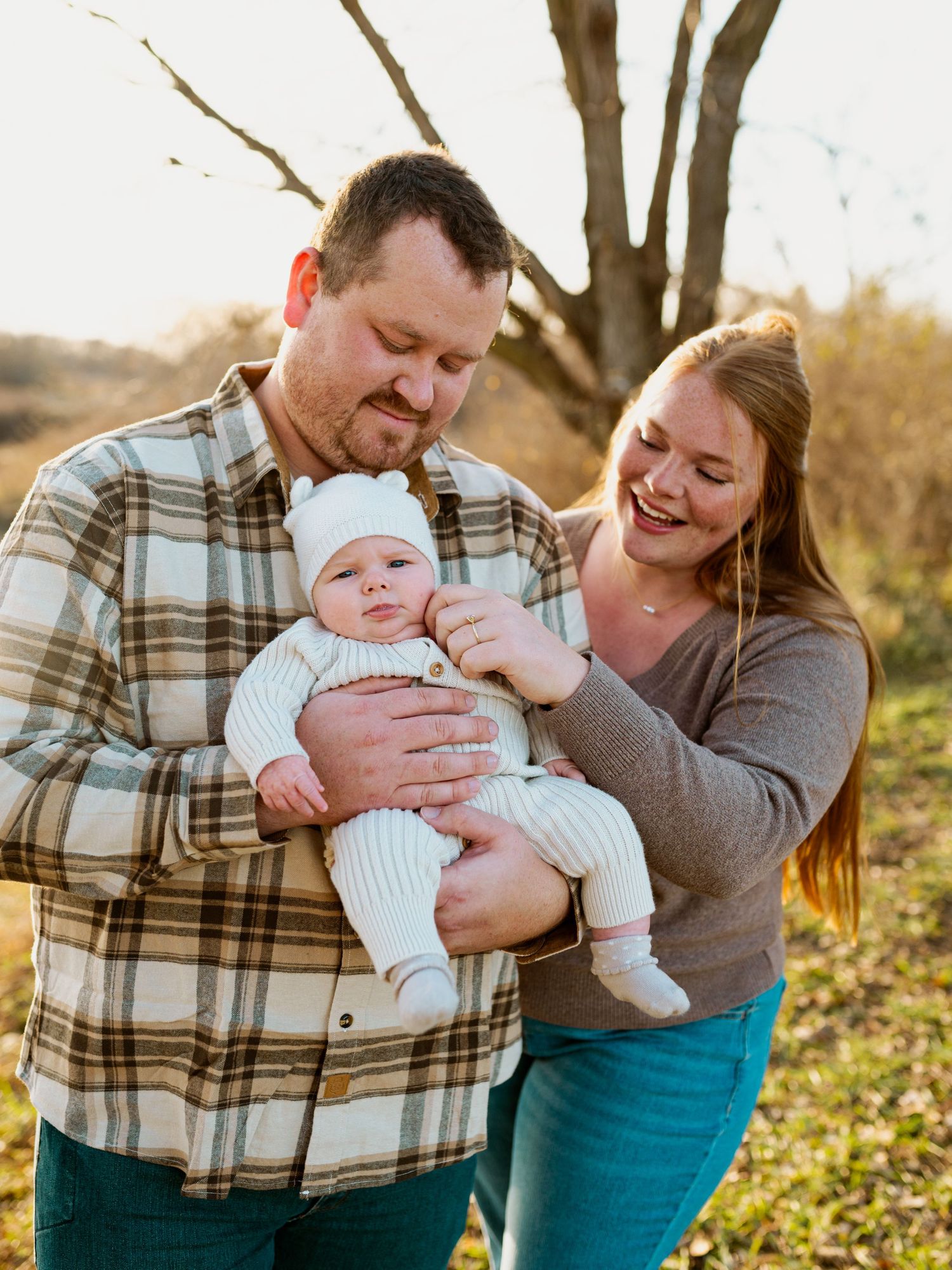 Parents in plaid and teal share joyful moments with their baby during an outdoor autumn photoshoot at sunset.