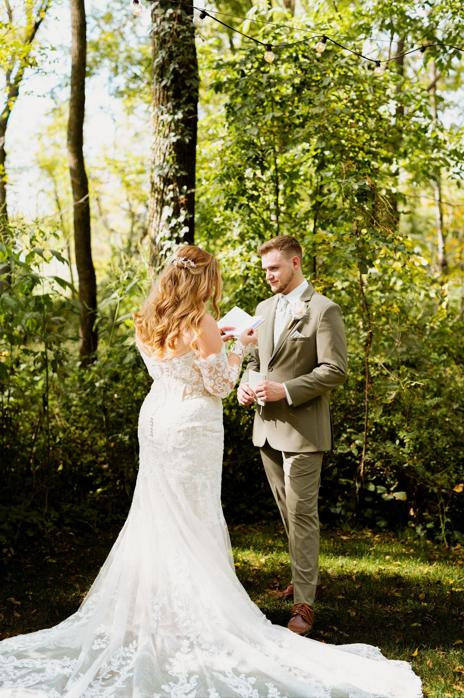 A couple shares their first look moment in a lush forest setting with the bride wearing a stunning lace wedding gown.