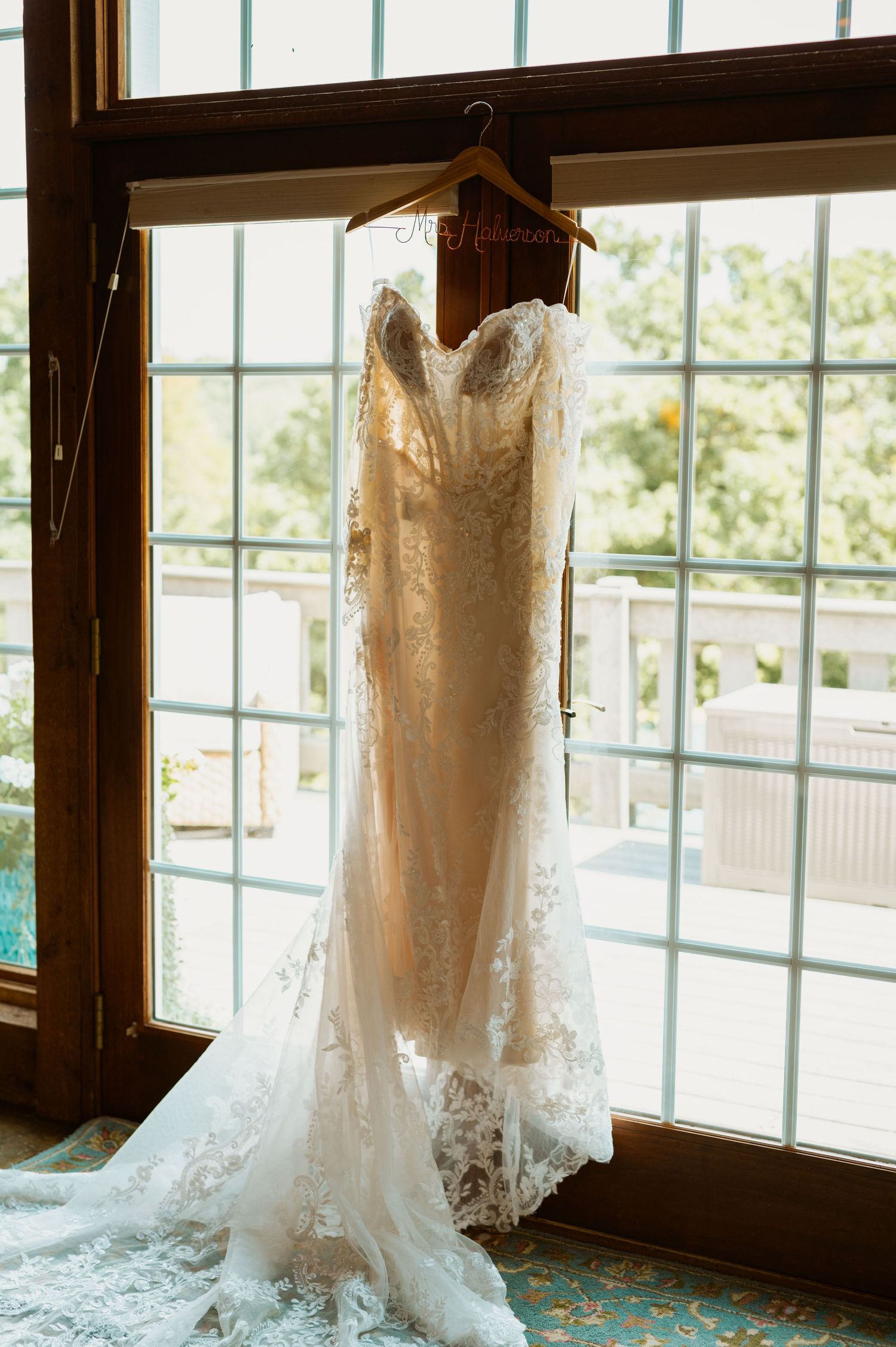 White lace wedding dress hanging by window with natural light streaming in.