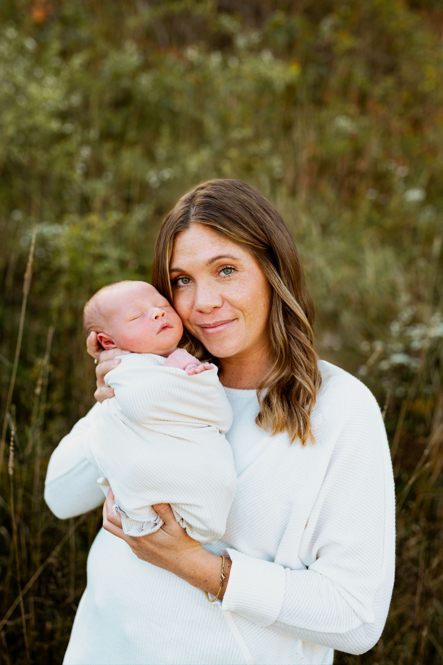 A series of tender moments between a woman in white and a newborn baby against a natural outdoor backdrop.