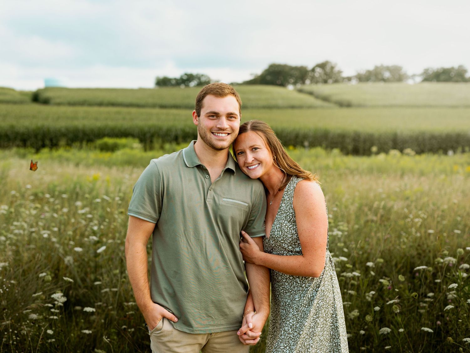 A couple embraces in a sunlit meadow filled with blooming white wildflowers on a summer afternoon.