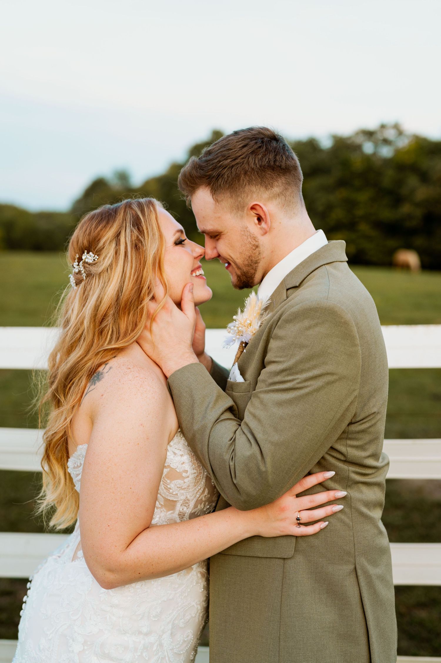 Joyful wedding couple sharing a laugh against white fence during sunset photo session.
