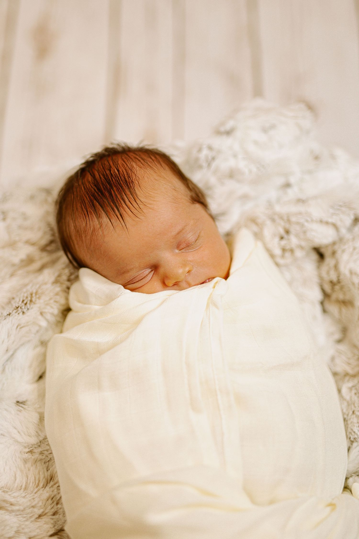 Sleeping newborn baby wrapped in white swaddle blanket on soft textured bedding.