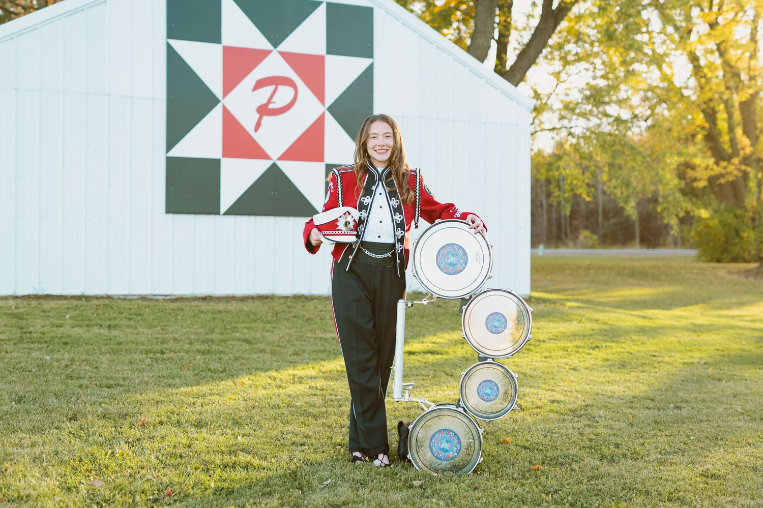 Marching band member stands with equipment by barn with decorative quilt pattern.
