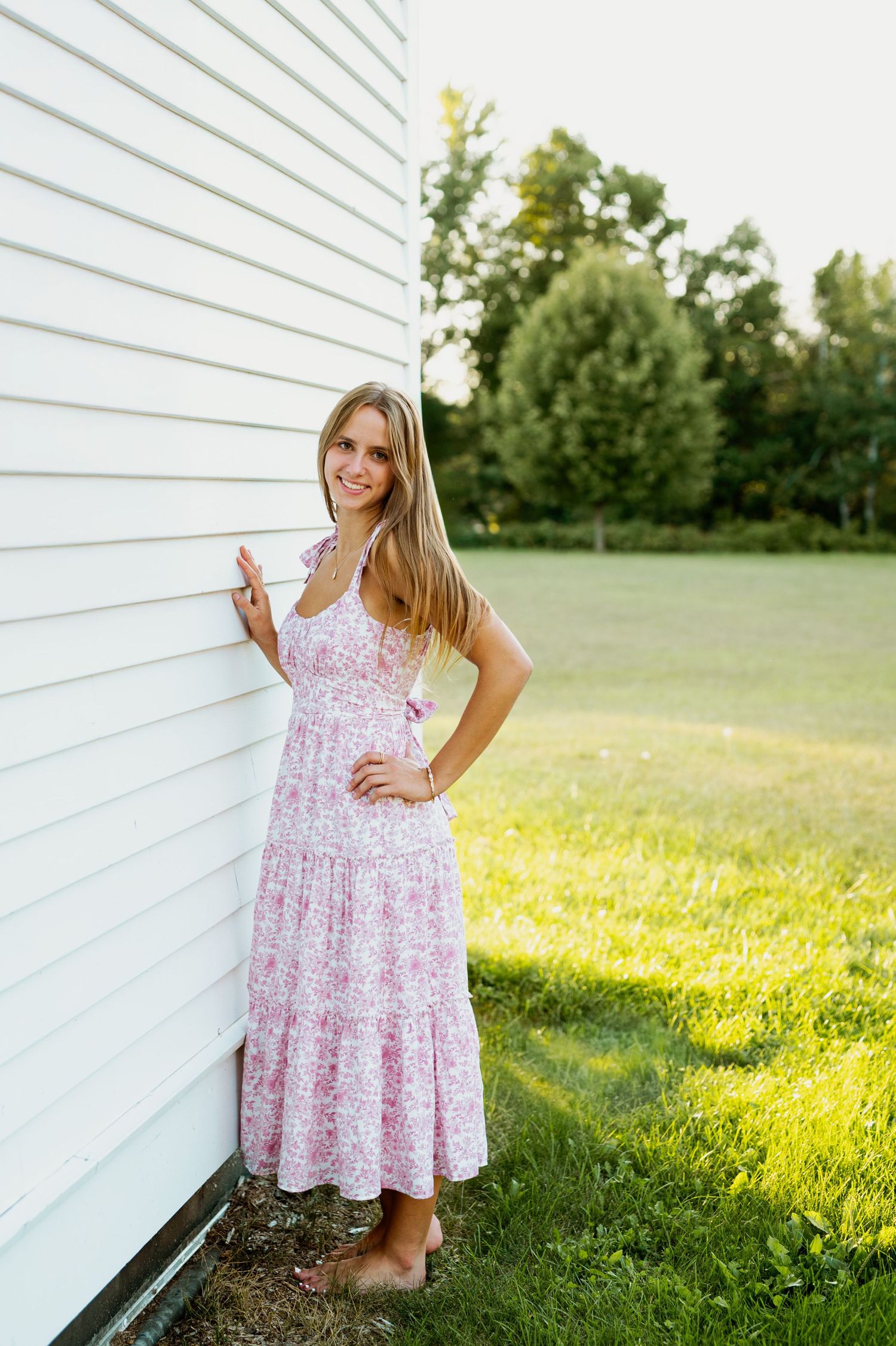A floral sundress is showcased against a white wall and green lawn in warm evening sunlight.