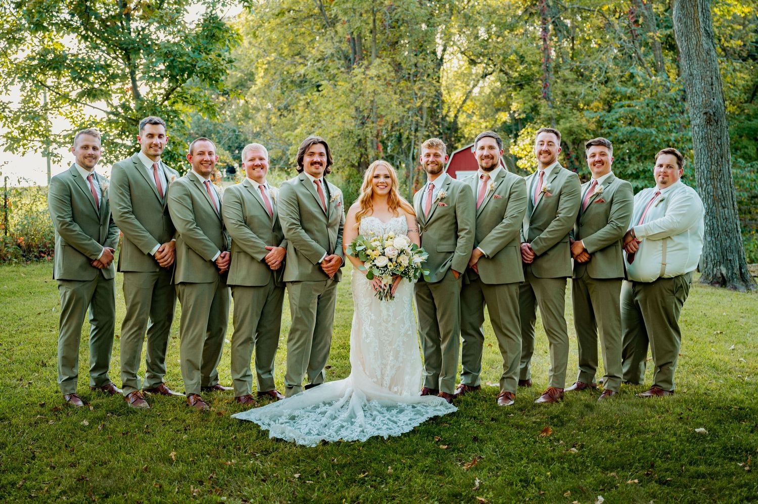 Wedding party in green and white attire posed on grassy hillside.