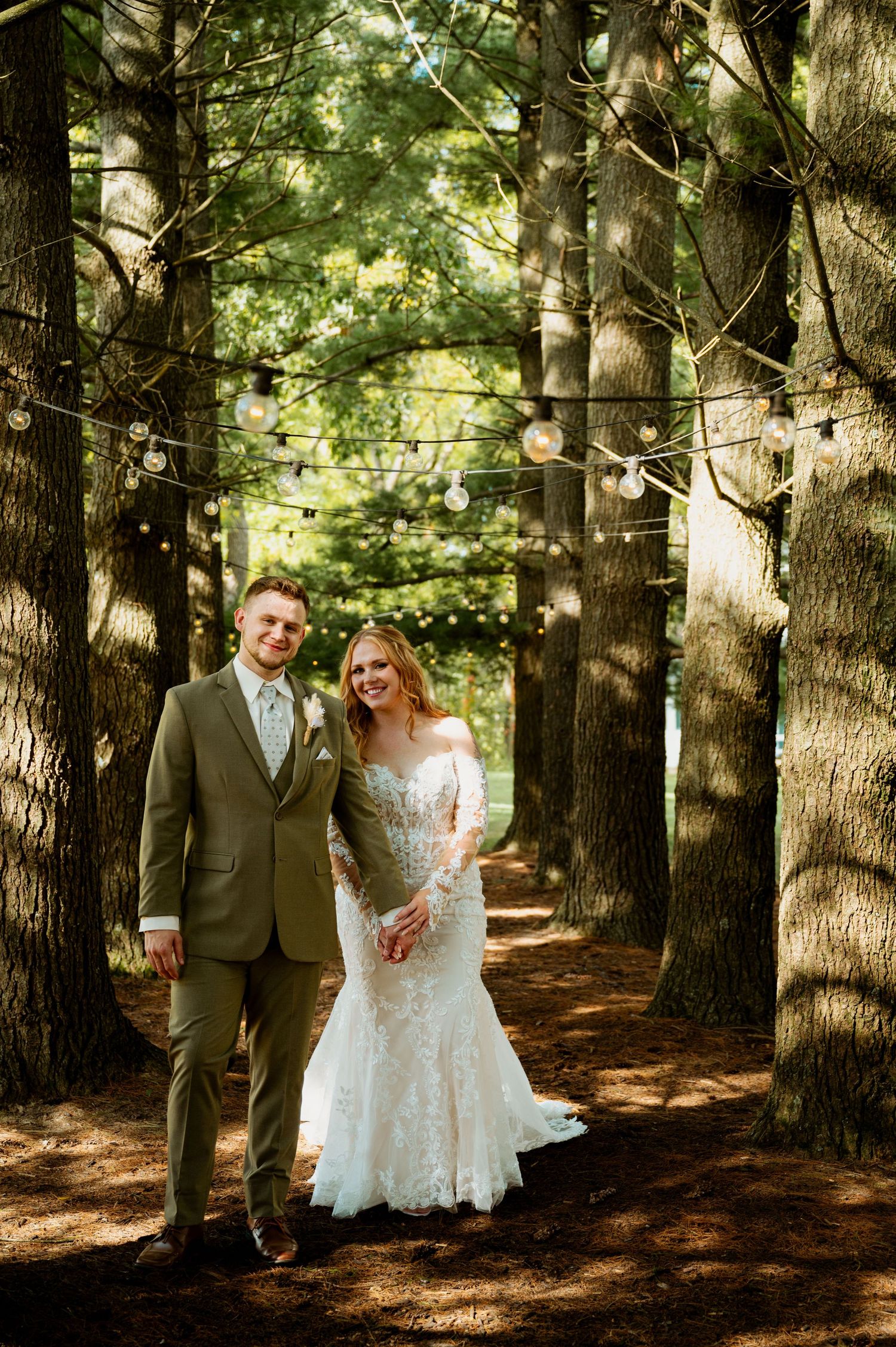 Newlyweds share joyful moments together in a sunlit pine forest setting.