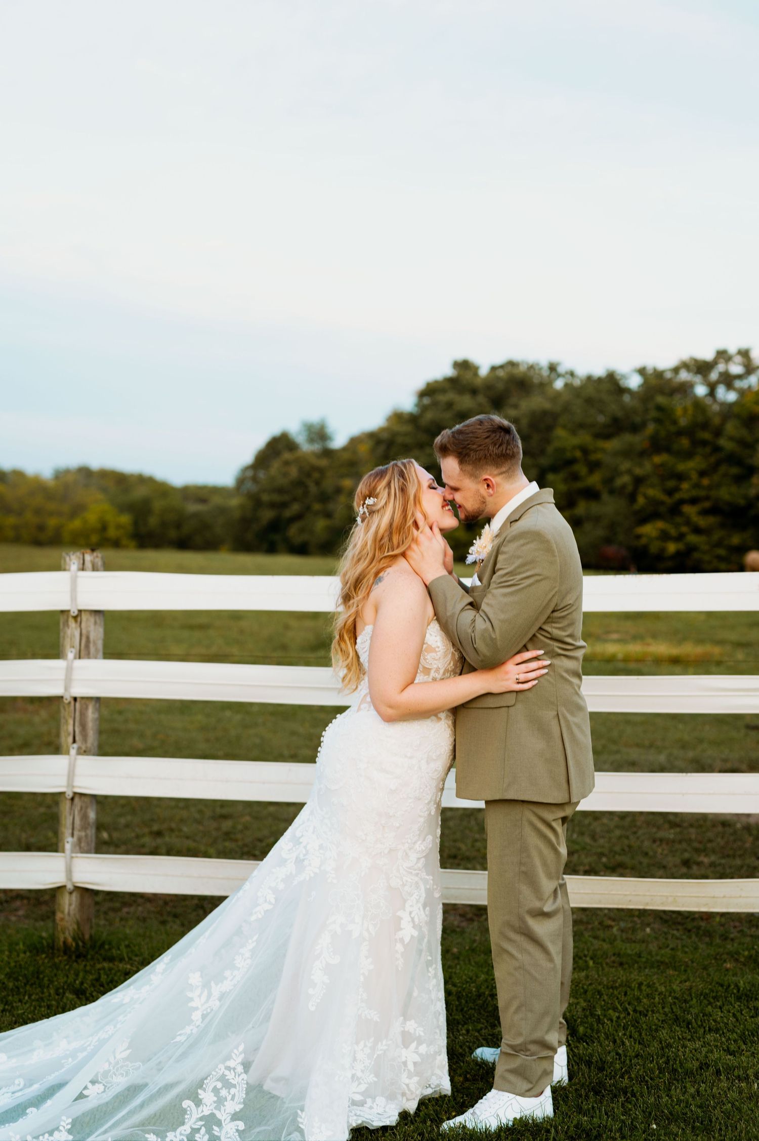 Elegant wedding portrait with white fence and rolling hills in background during golden hour.