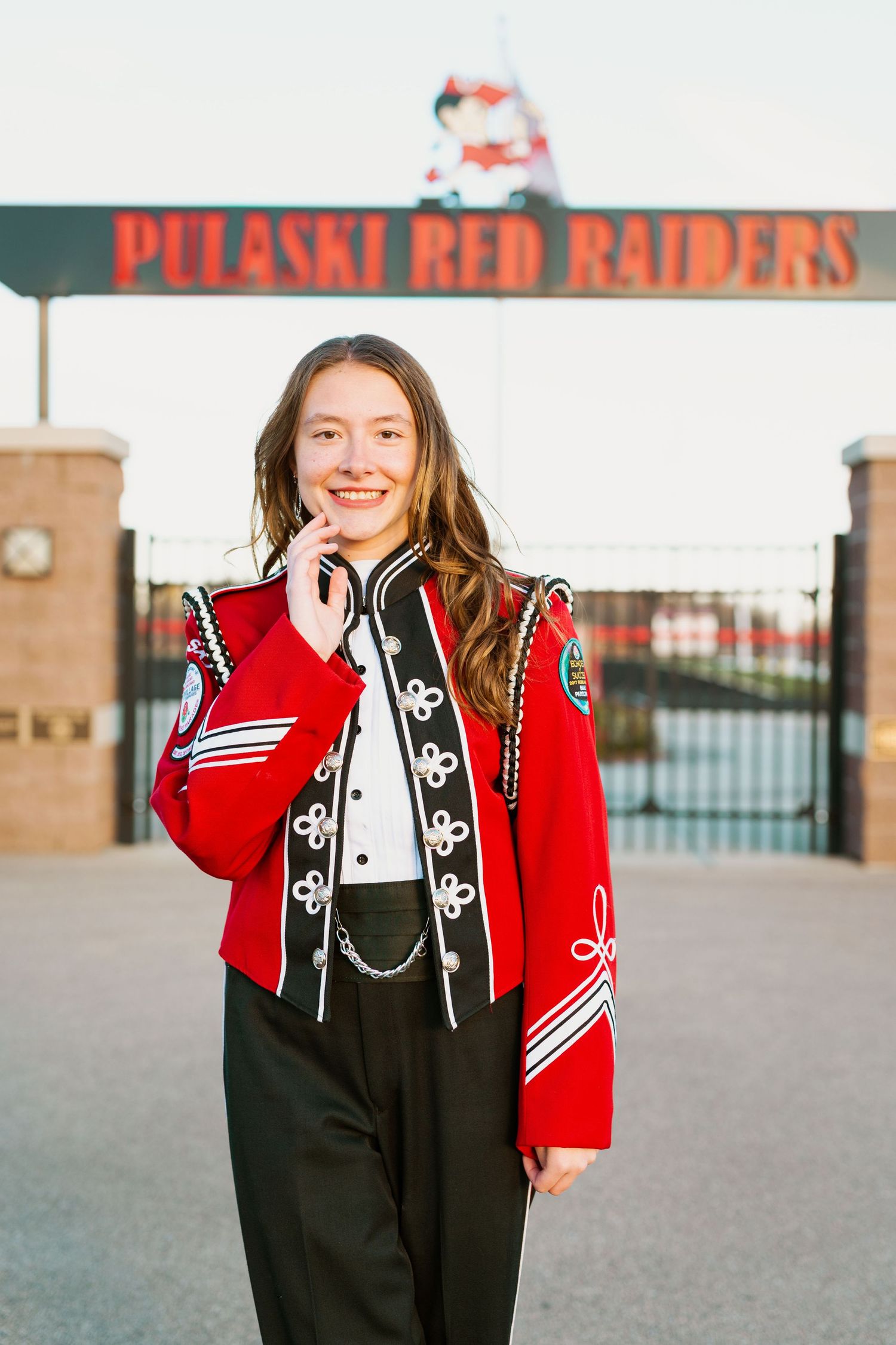 Band member in red uniform jacket poses at stadium entrance.