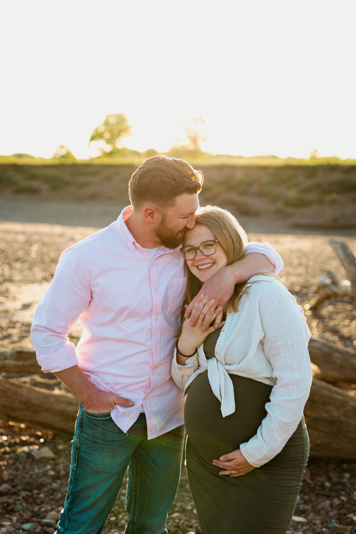 A tender outdoor couple's portrait at sunset with a warm embrace and smiles in golden light.