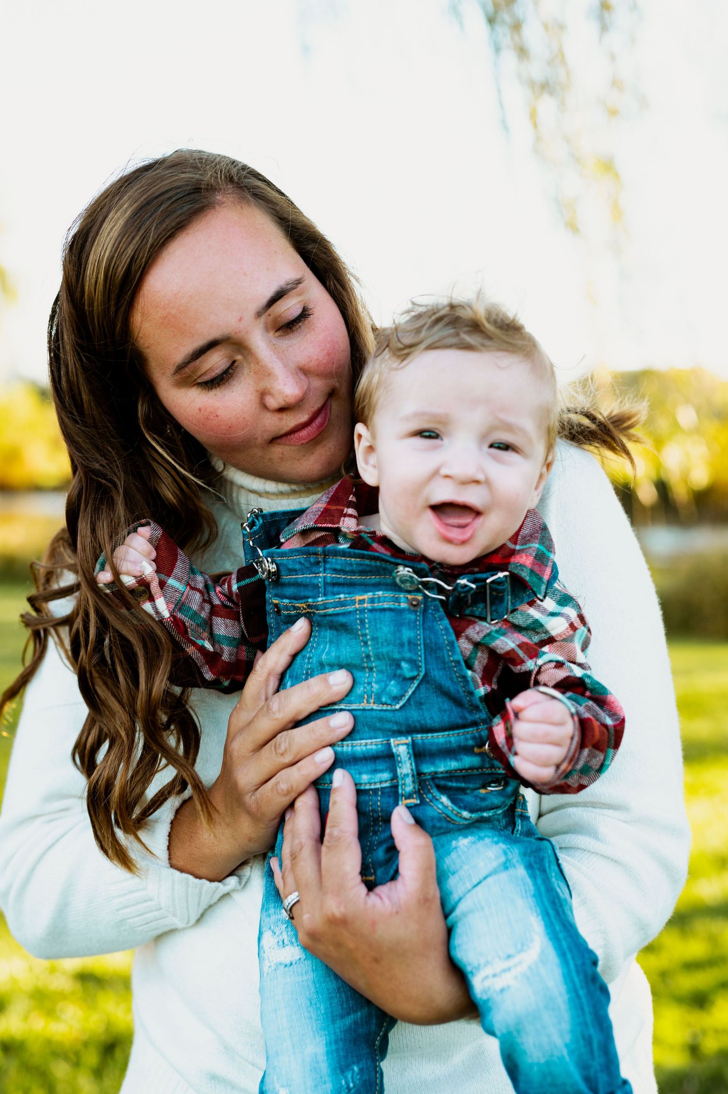 Parent and child share joyful cuddles and laughter while playing outdoors in casual attire.