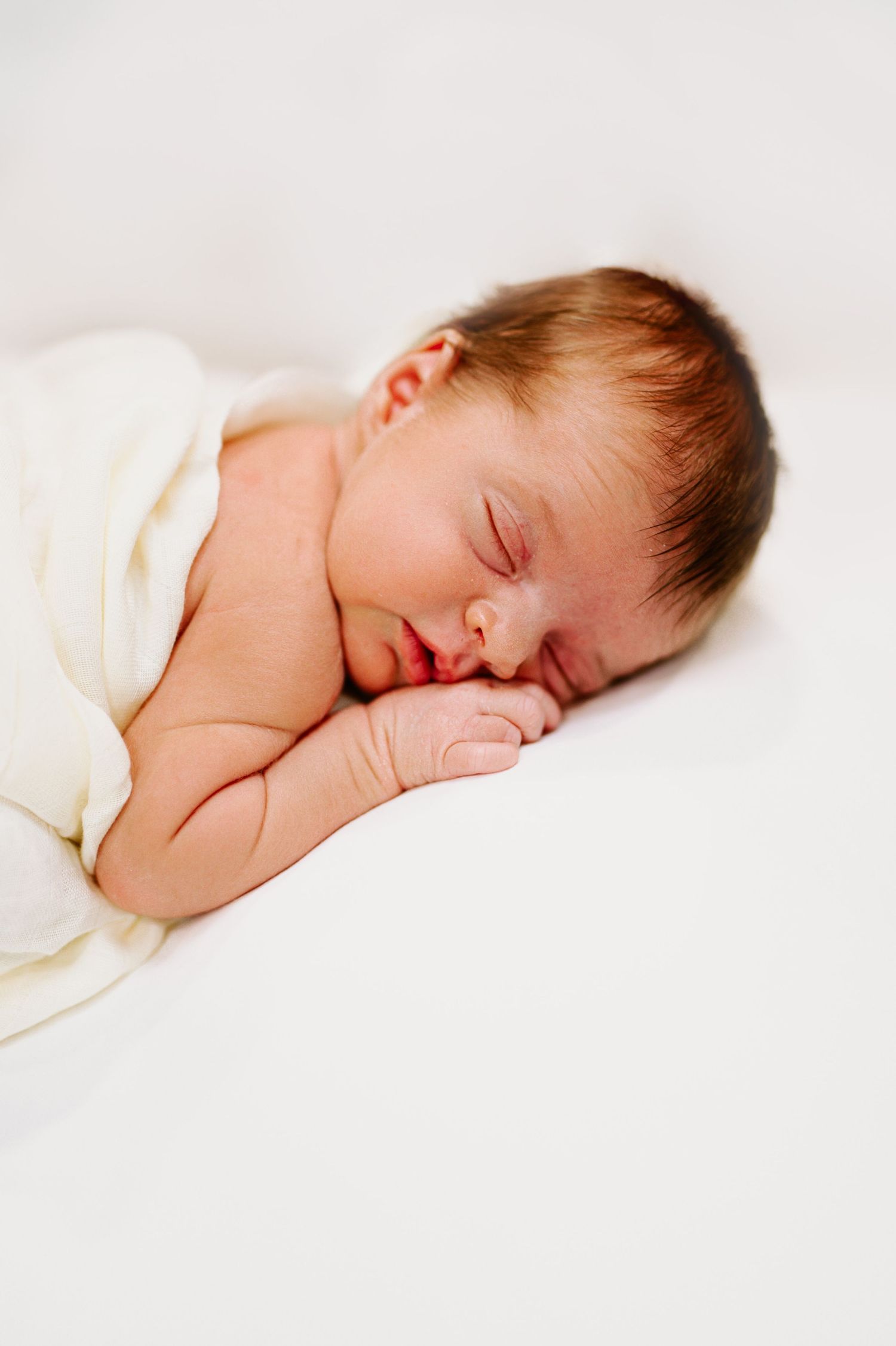 Sleeping newborn baby wrapped in soft white blanket.