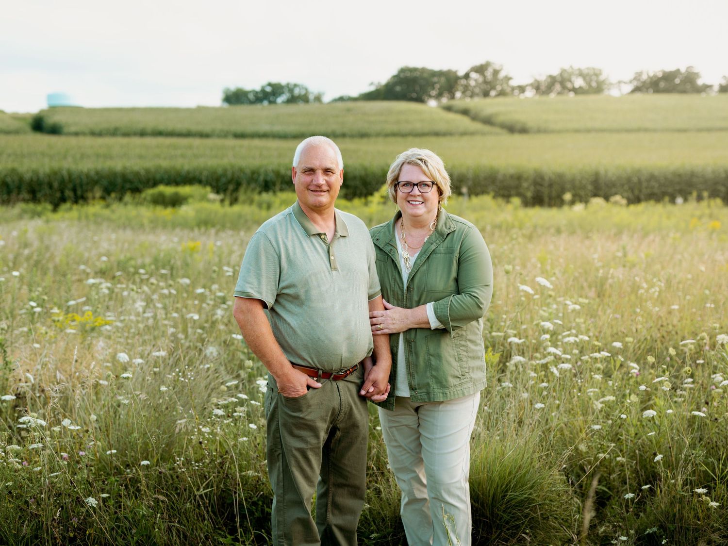 A couple stands together in a summer meadow filled with wildflowers during golden hour.