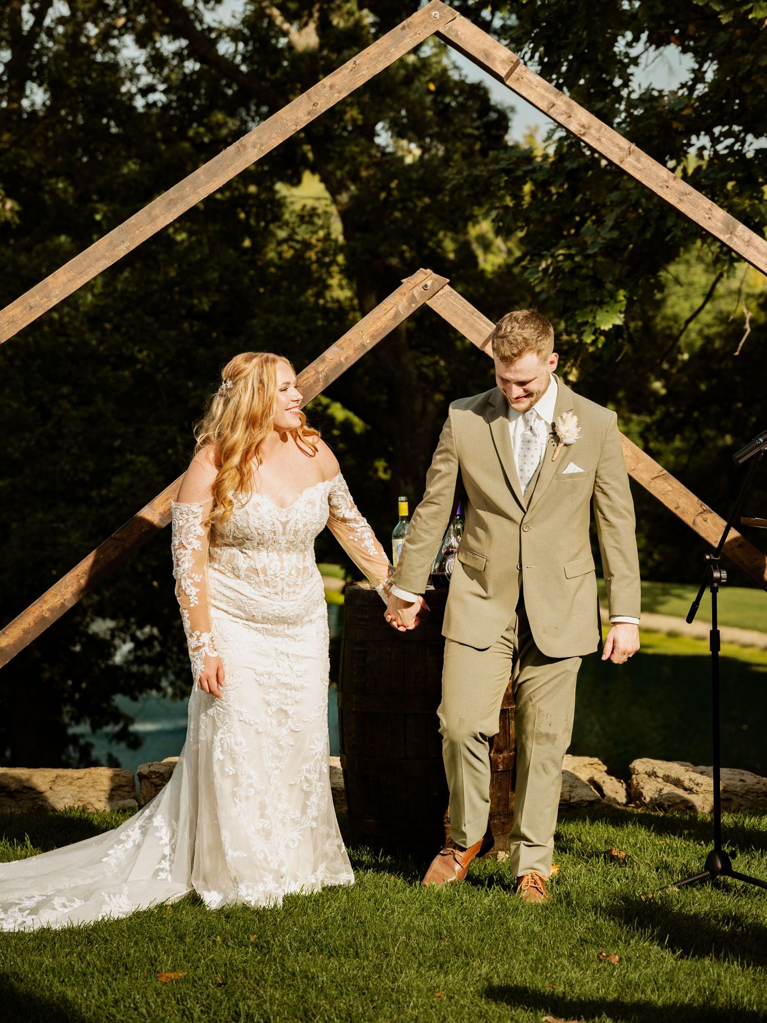 Wedding couple walking together on grassy hill with wooden architectural details.