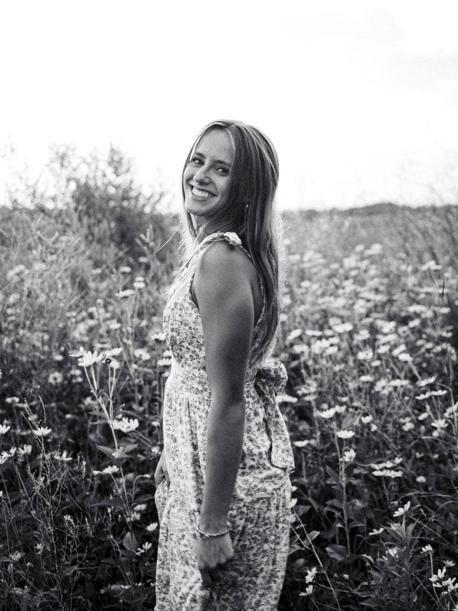 A woman in a floral dress poses joyfully in a meadow of wildflowers in black and white photography.