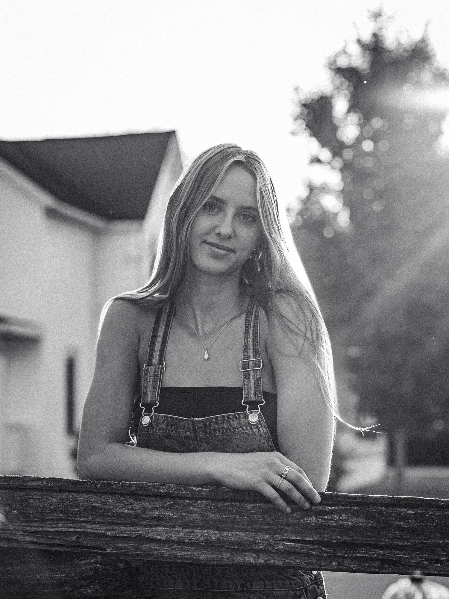 Black and white photo series showing someone in overalls leaning against a rustic wooden fence at sunset.