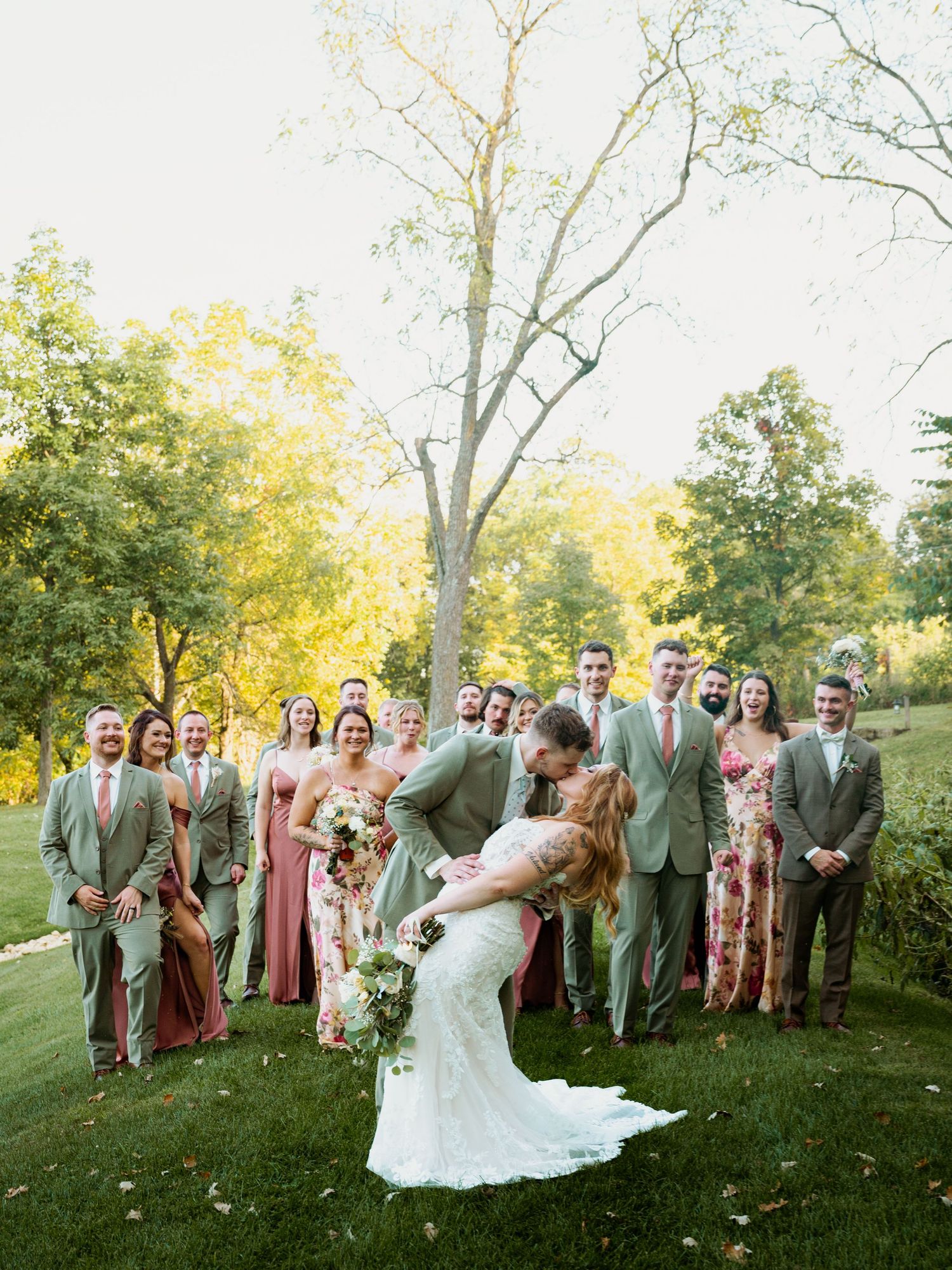 Wedding party celebrates outdoors with bridesmaids in dusty rose dresses and groomsmen in sage green suits.