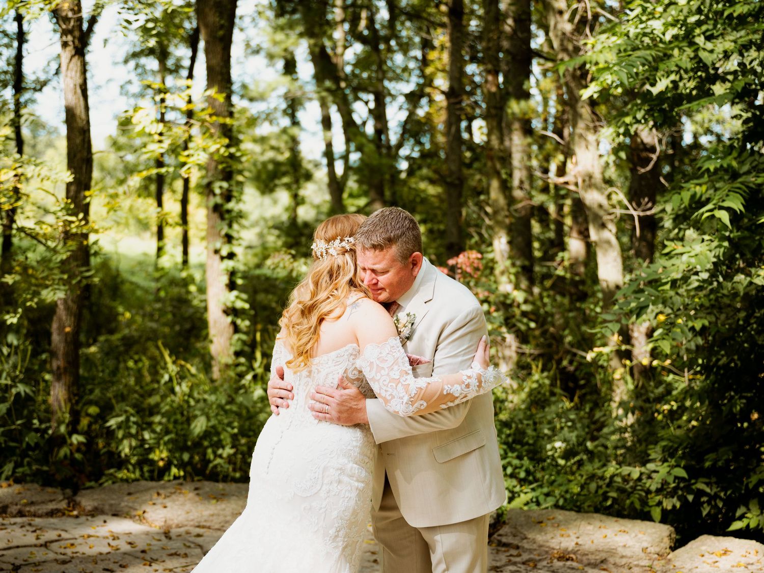 Wedding couple embracing in sunlit wooded setting.