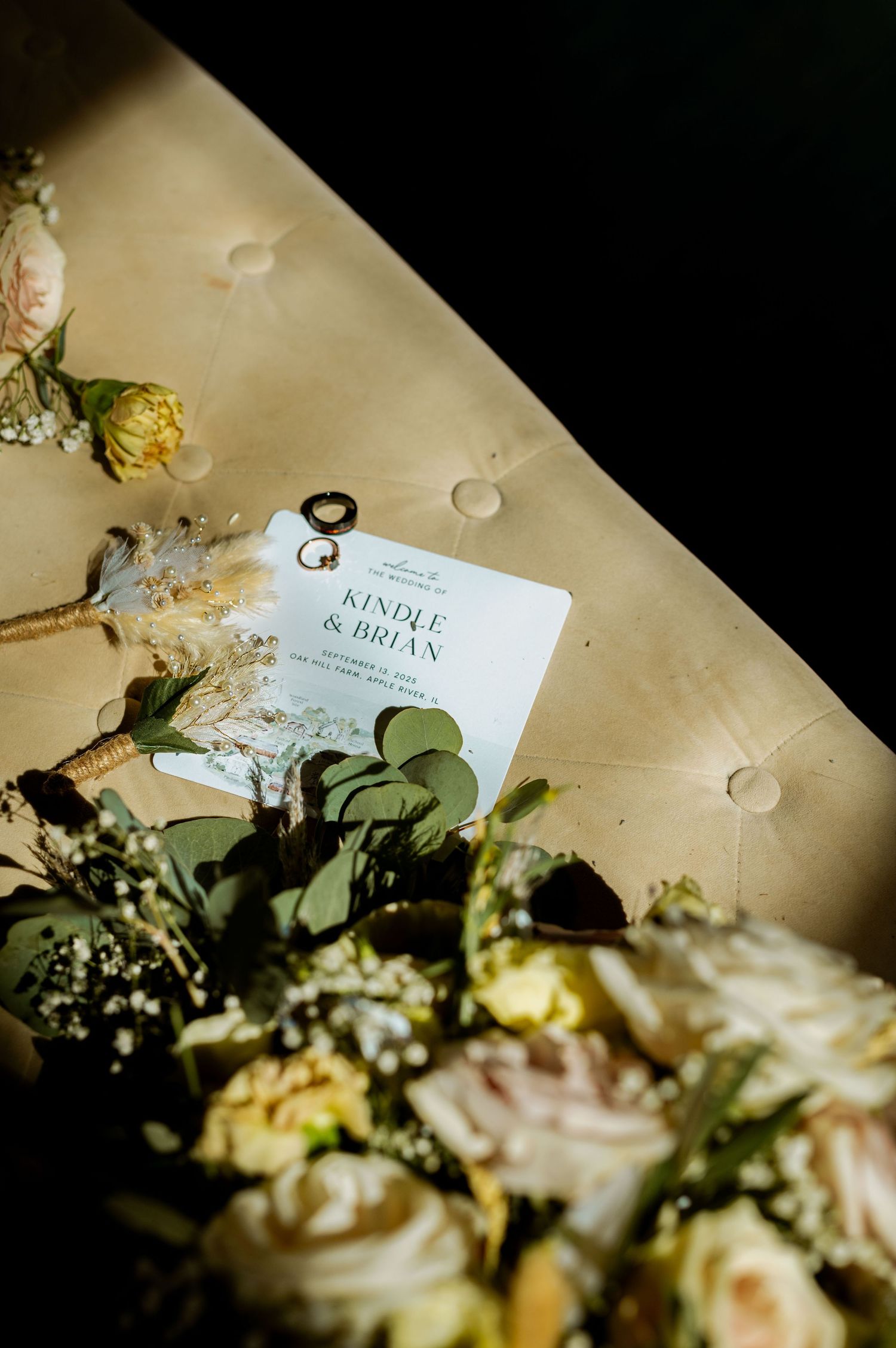 Wedding invitation and delicate roses arranged on a tufted beige surface in soft lighting.