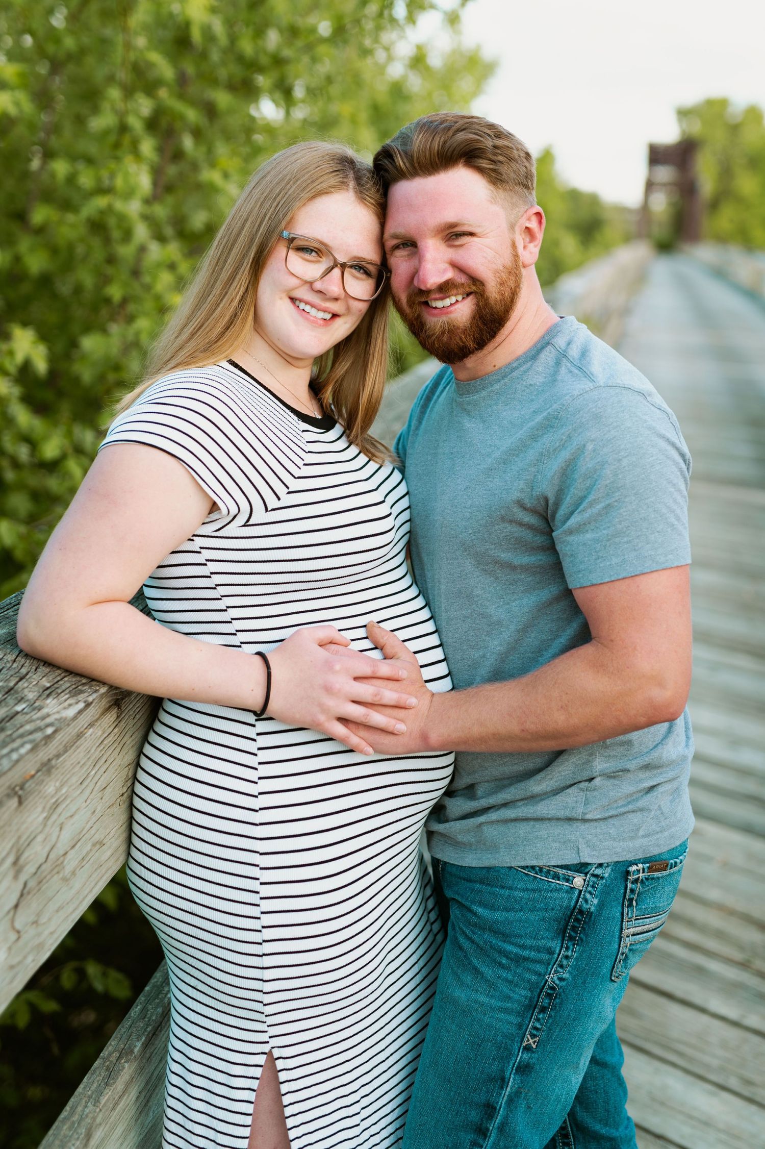 Couple in casual attire smiling and embracing on wooden boardwalk.