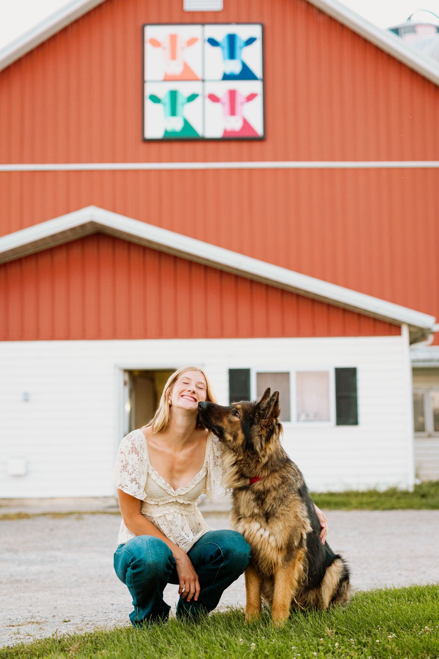 A joyful interaction between a person and a German Shepherd dog on a grassy lawn in front of an orange barn.